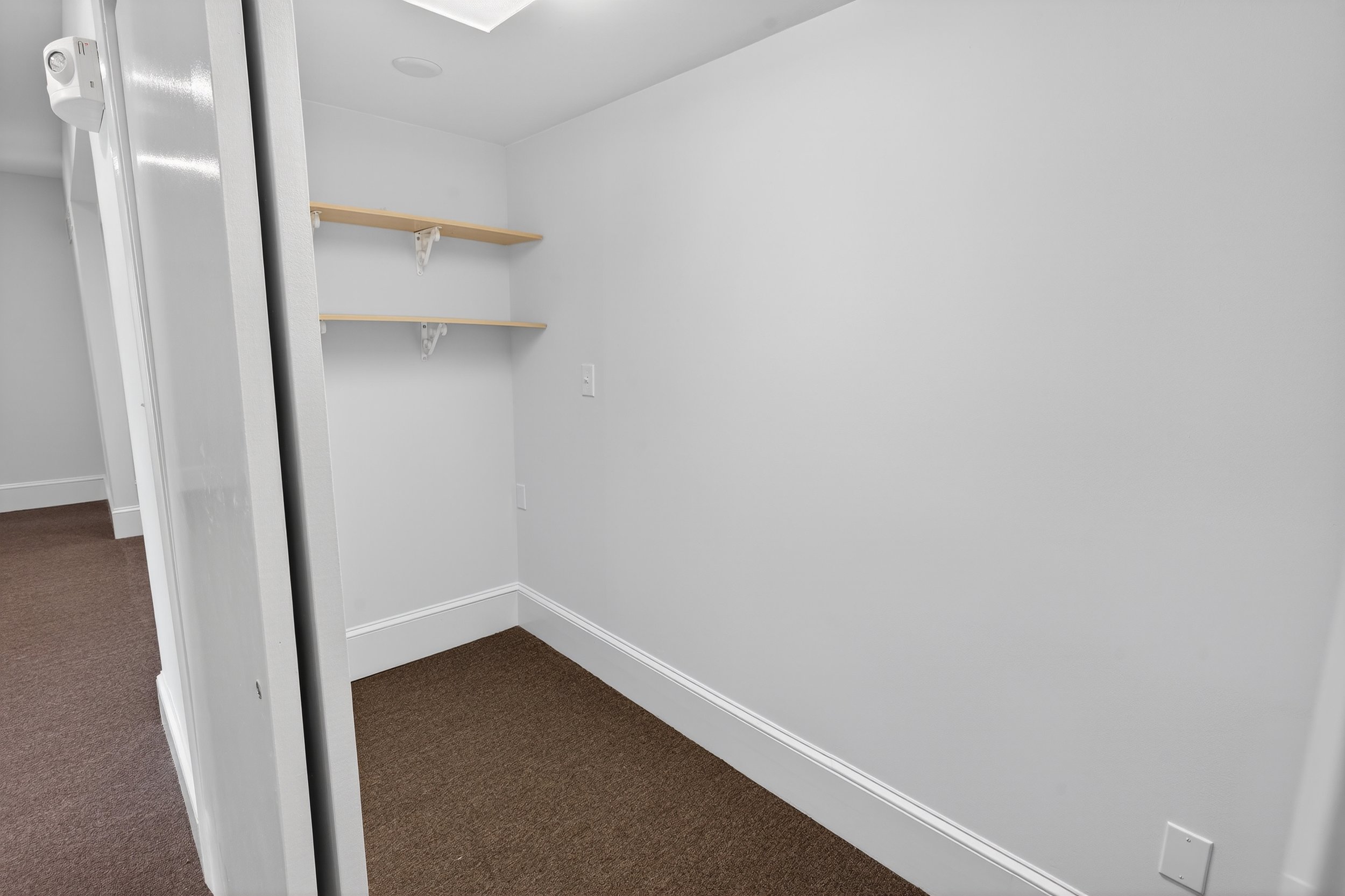 Empty room with two wooden shelves on the wall and brown carpeted floor.