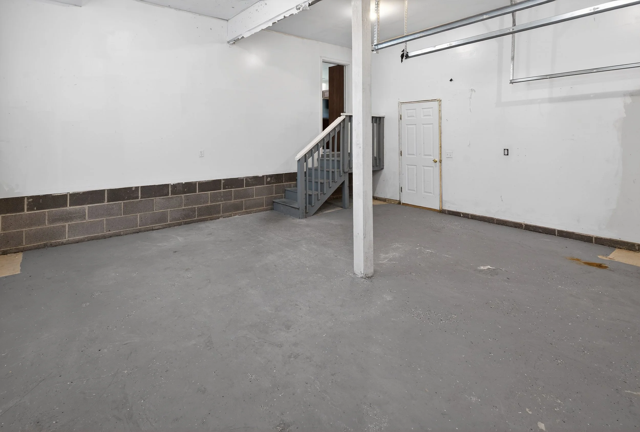 Empty unfinished garage with gray concrete floor, white walls, and a small staircase leading to a doorway.