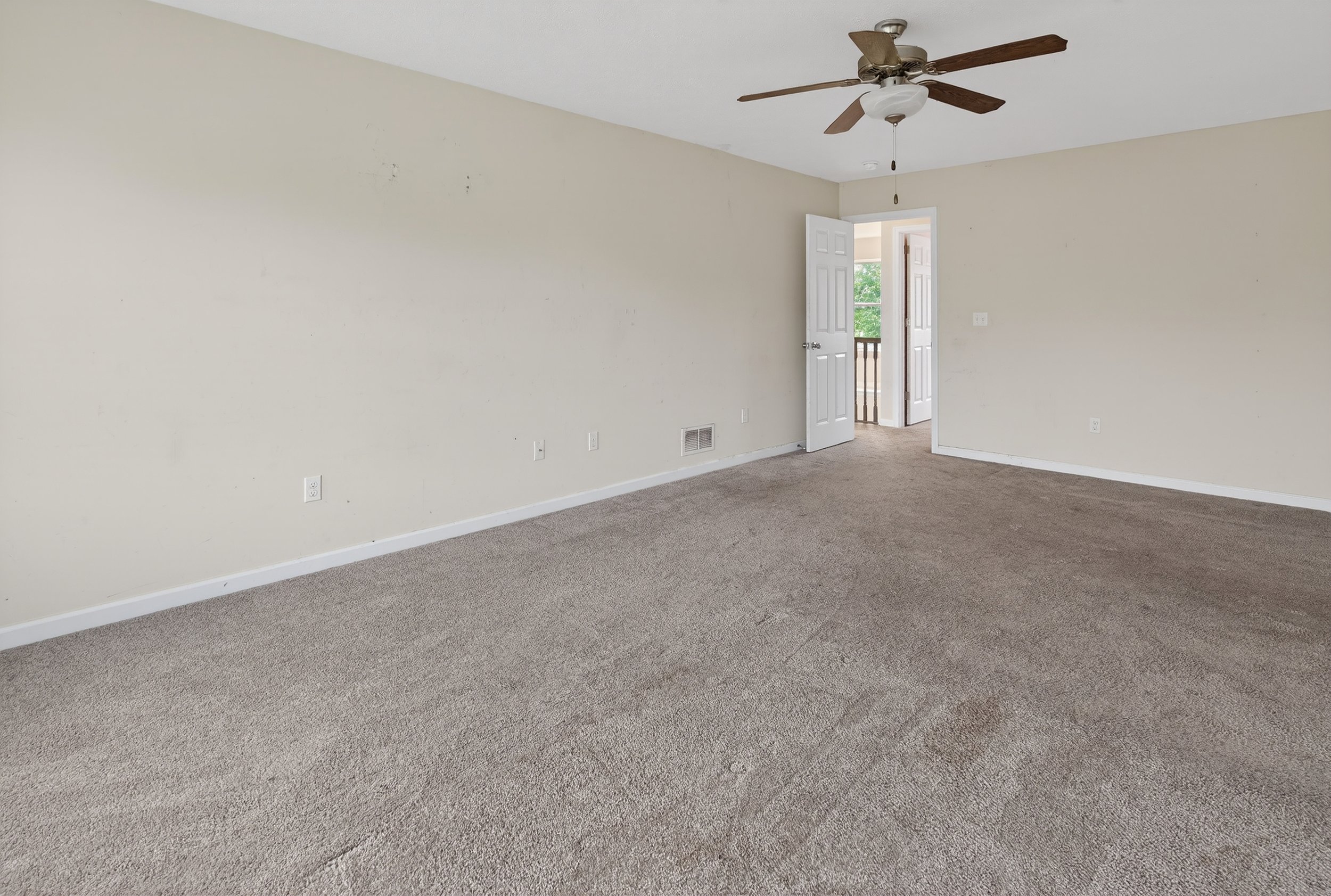 Empty room with beige walls, brown carpet, a ceiling fan, and an open door leading to a balcony.