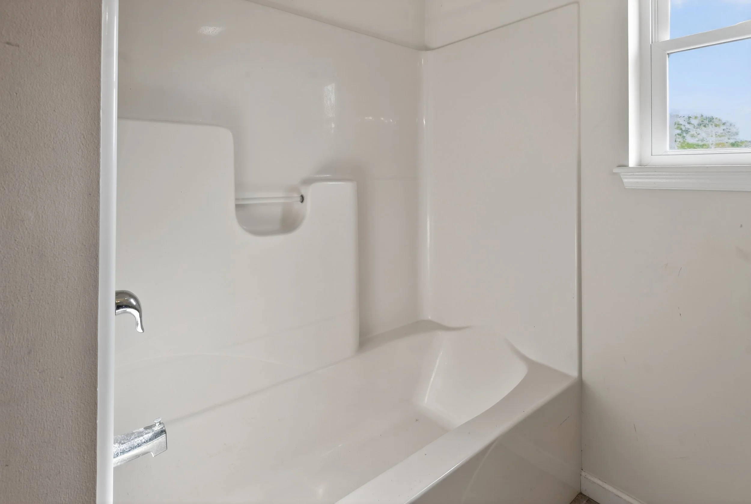 Empty white bathtub with a small window showing a blue sky and some greenery outside.