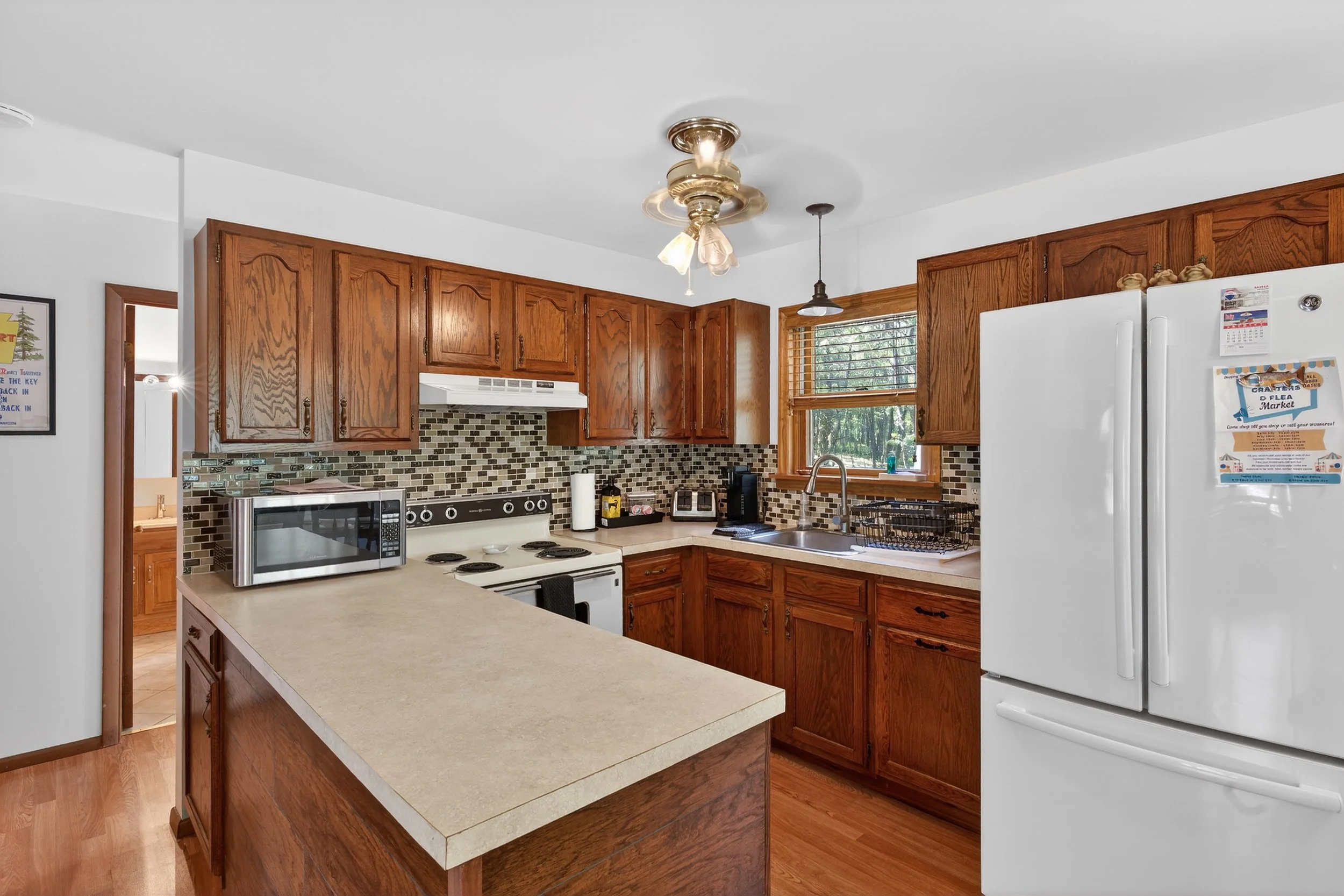 Kitchen with wooden cabinets, white refrigerator, microwave, stove, and sink by window with blinds.