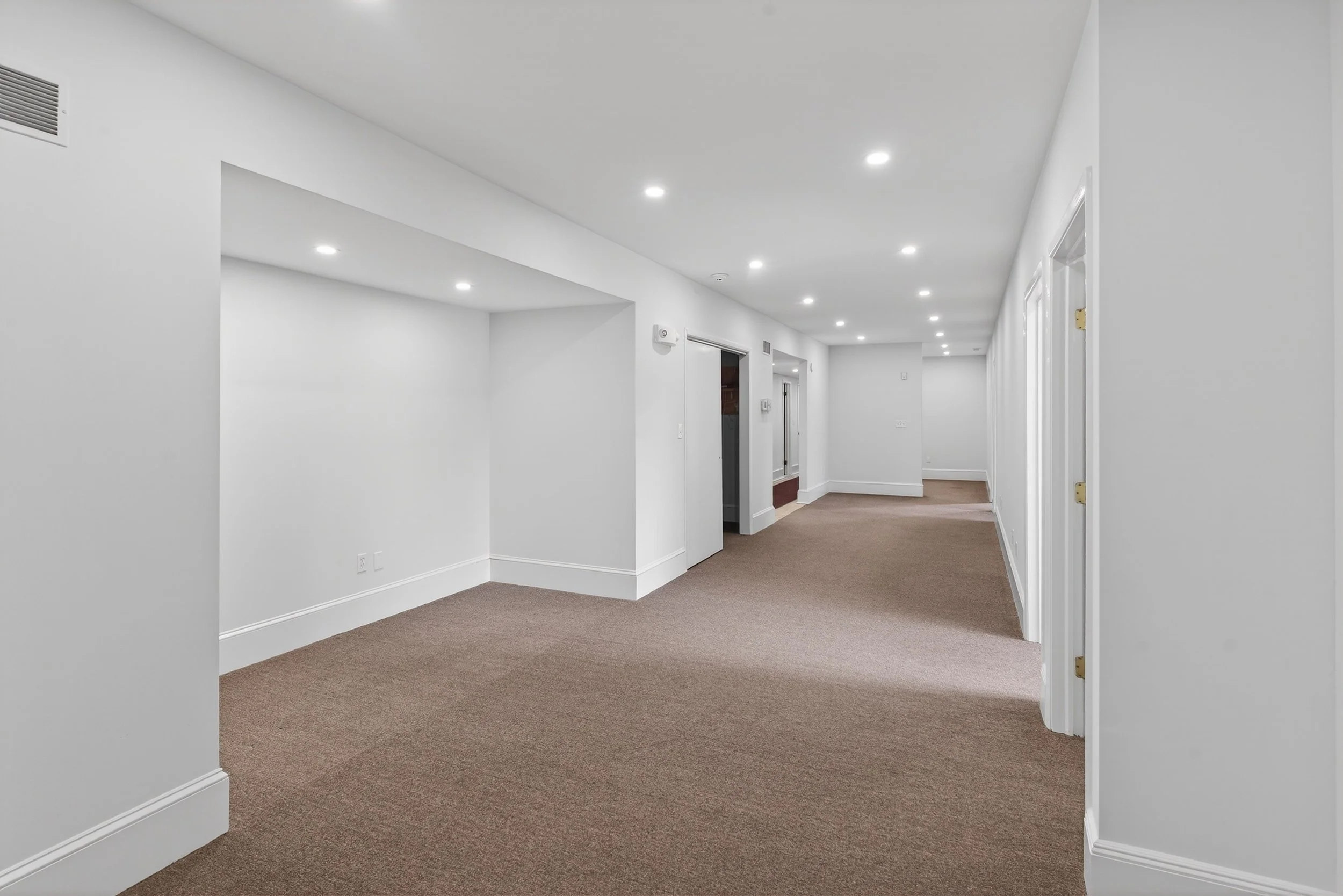 Empty hallway with beige carpet, white walls, and white ceiling with recessed lighting.