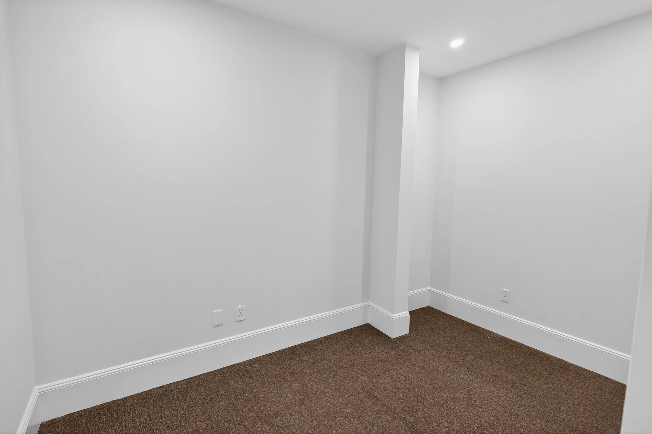 Empty room with white walls, brown carpet flooring, and electrical outlets.