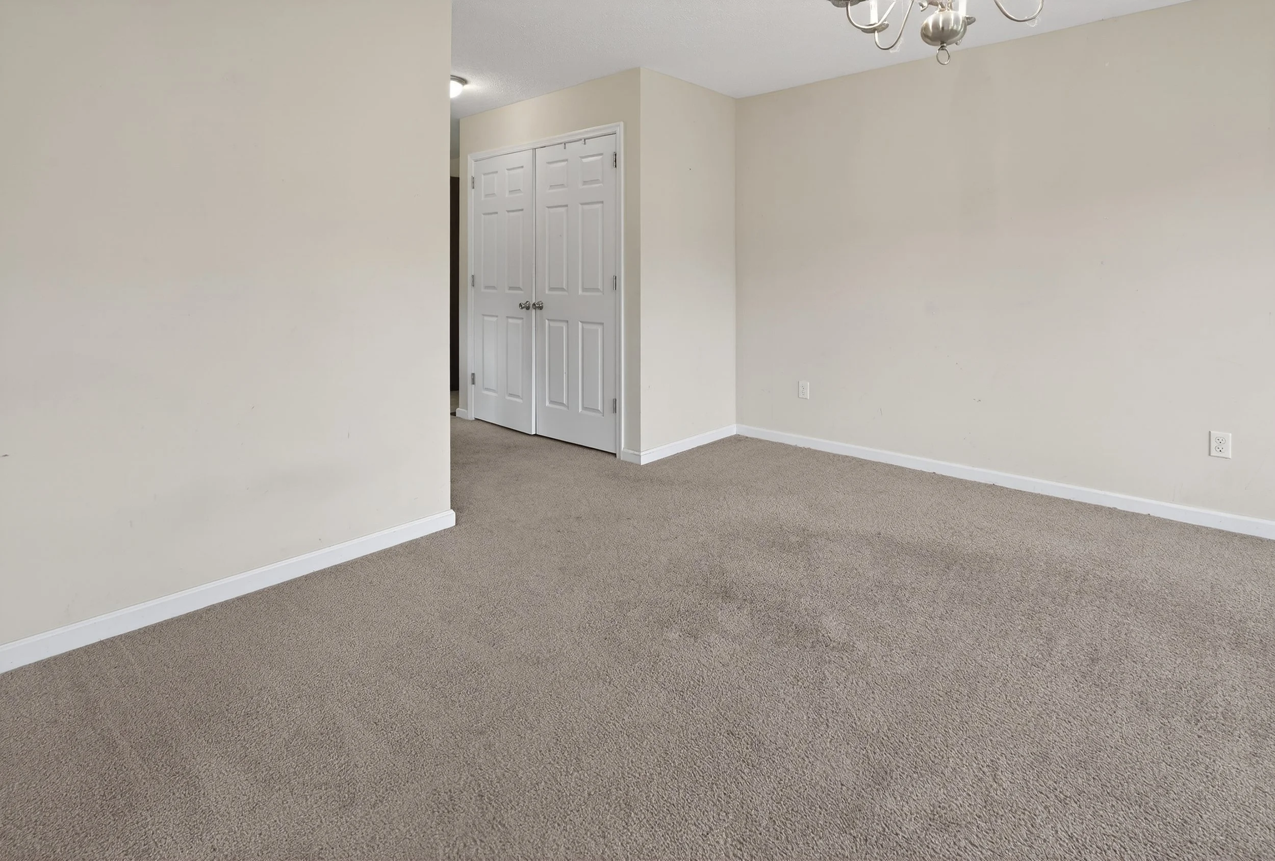 Empty room with beige carpet, white walls, a white ceiling, and double closet doors.