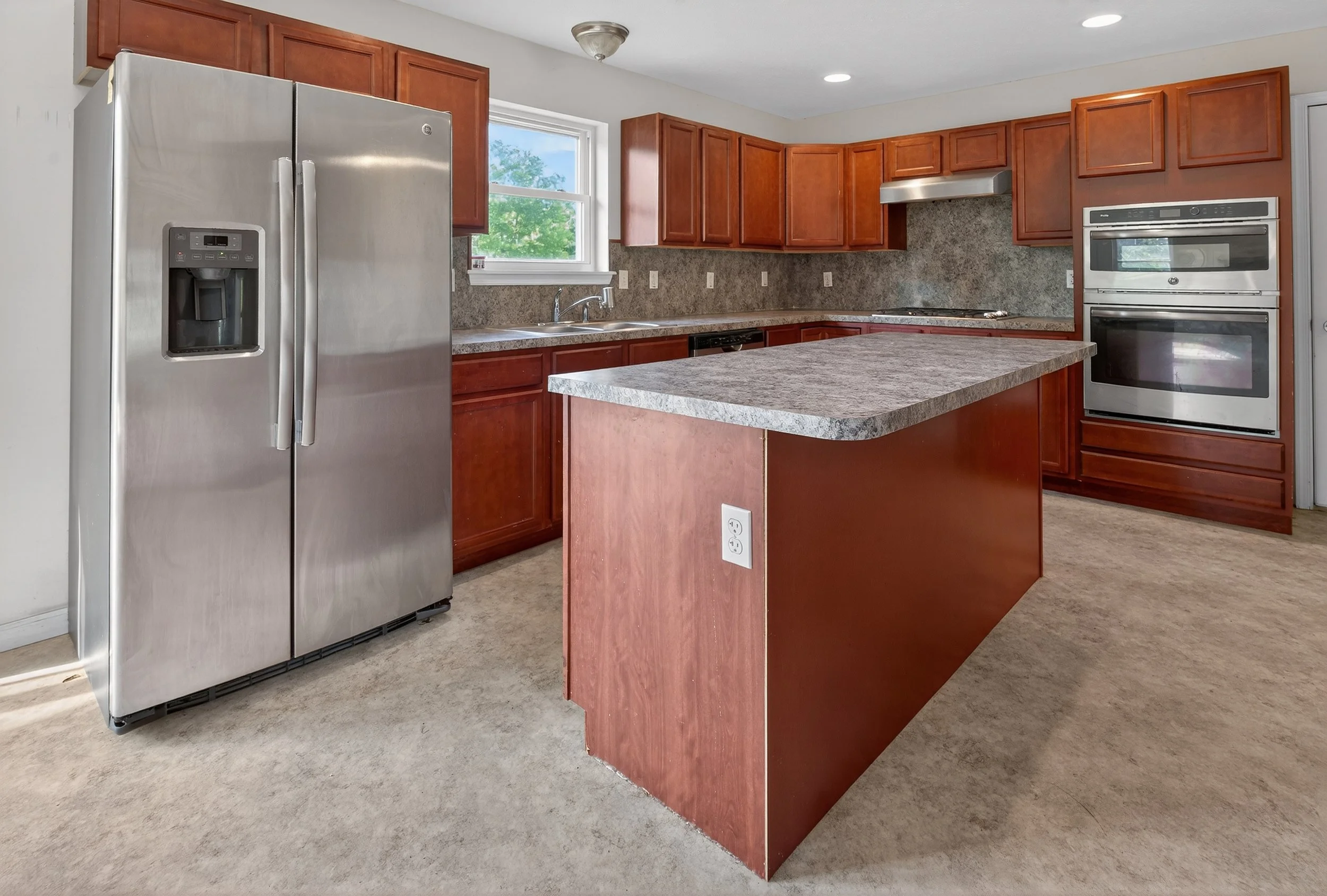 Kitchen with wooden cabinets, stainless steel refrigerator, double oven, and central island with a power outlet.