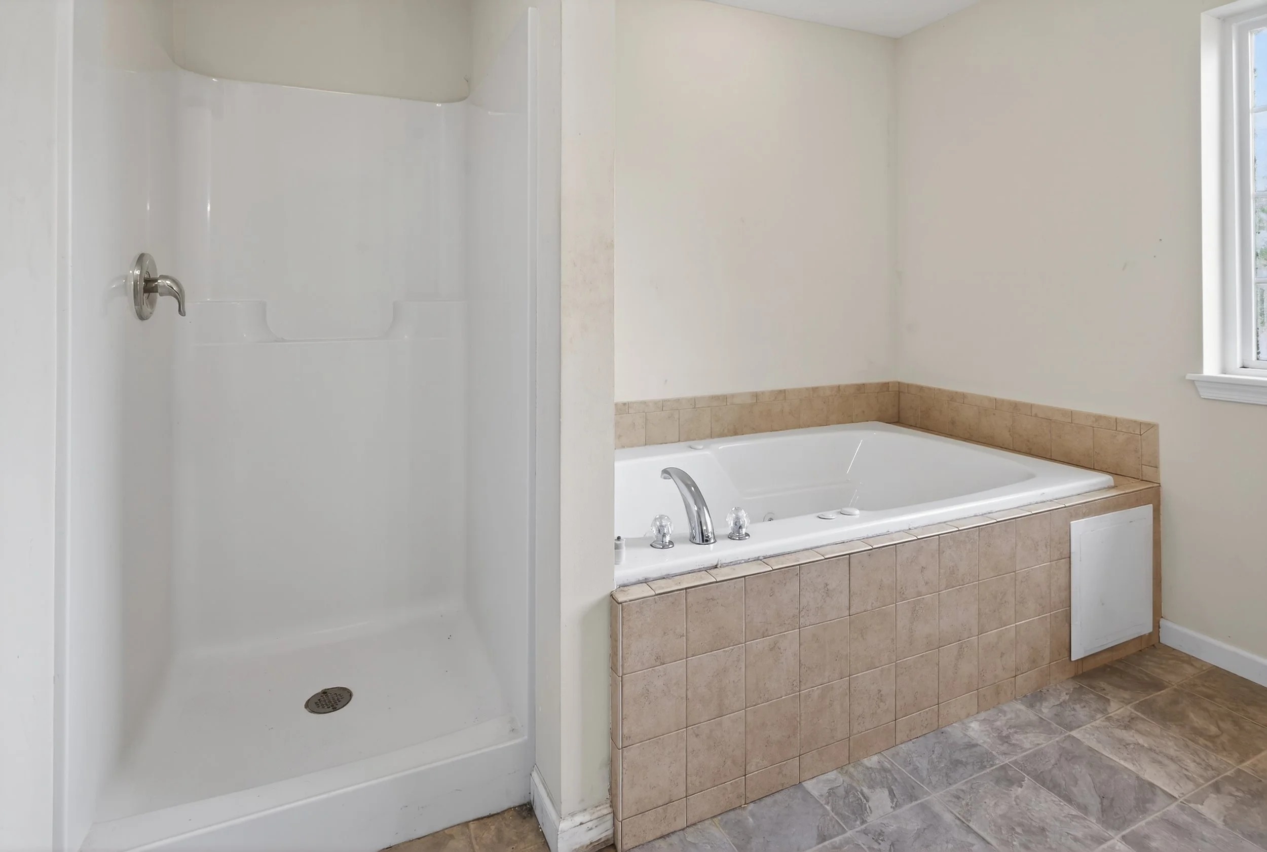 Bathroom featuring a walk-in shower on the left and a large built-in bathtub with beige tiles on the right, next to a window.