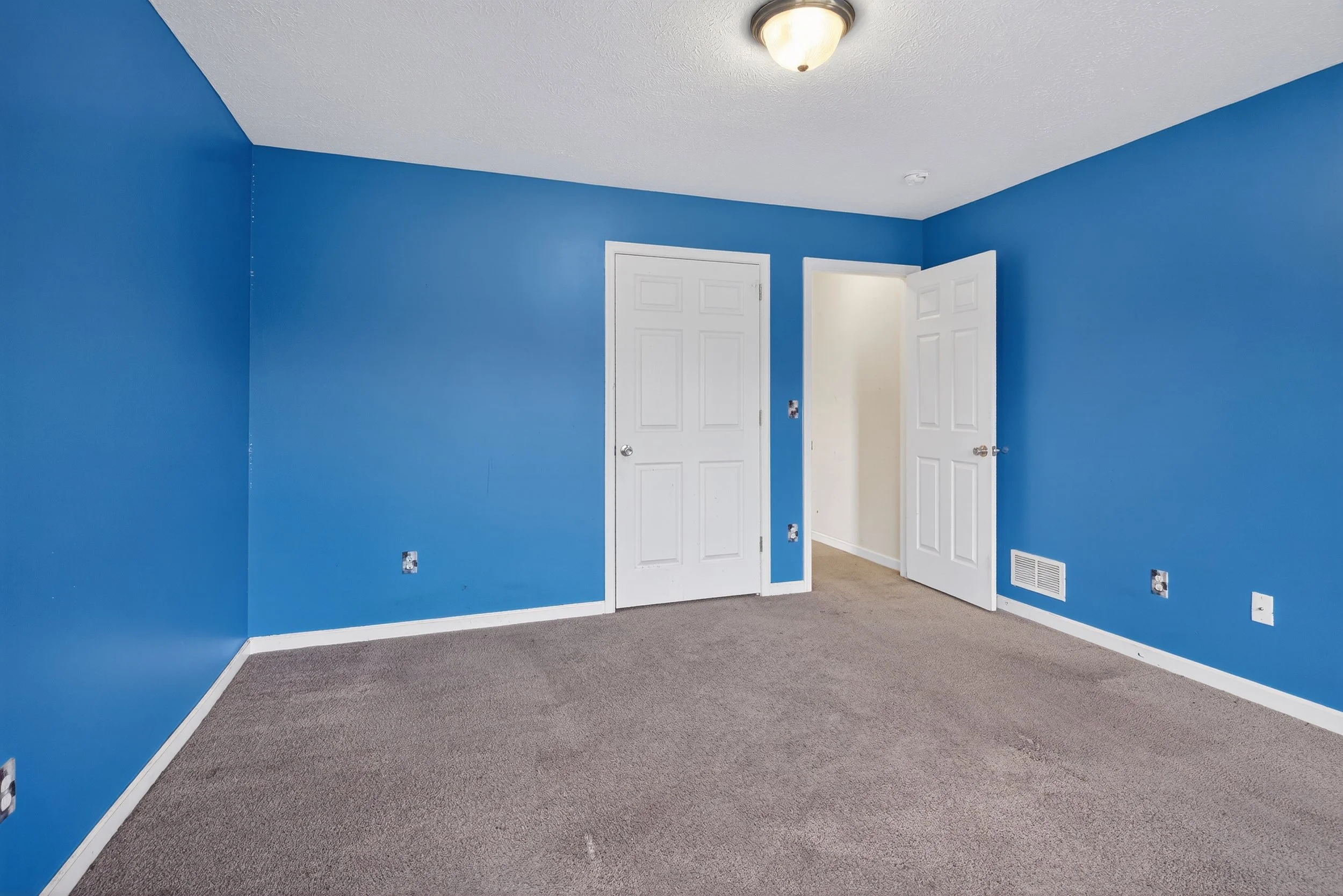Empty room with blue walls, white doors, beige carpet, and ceiling light fixture.