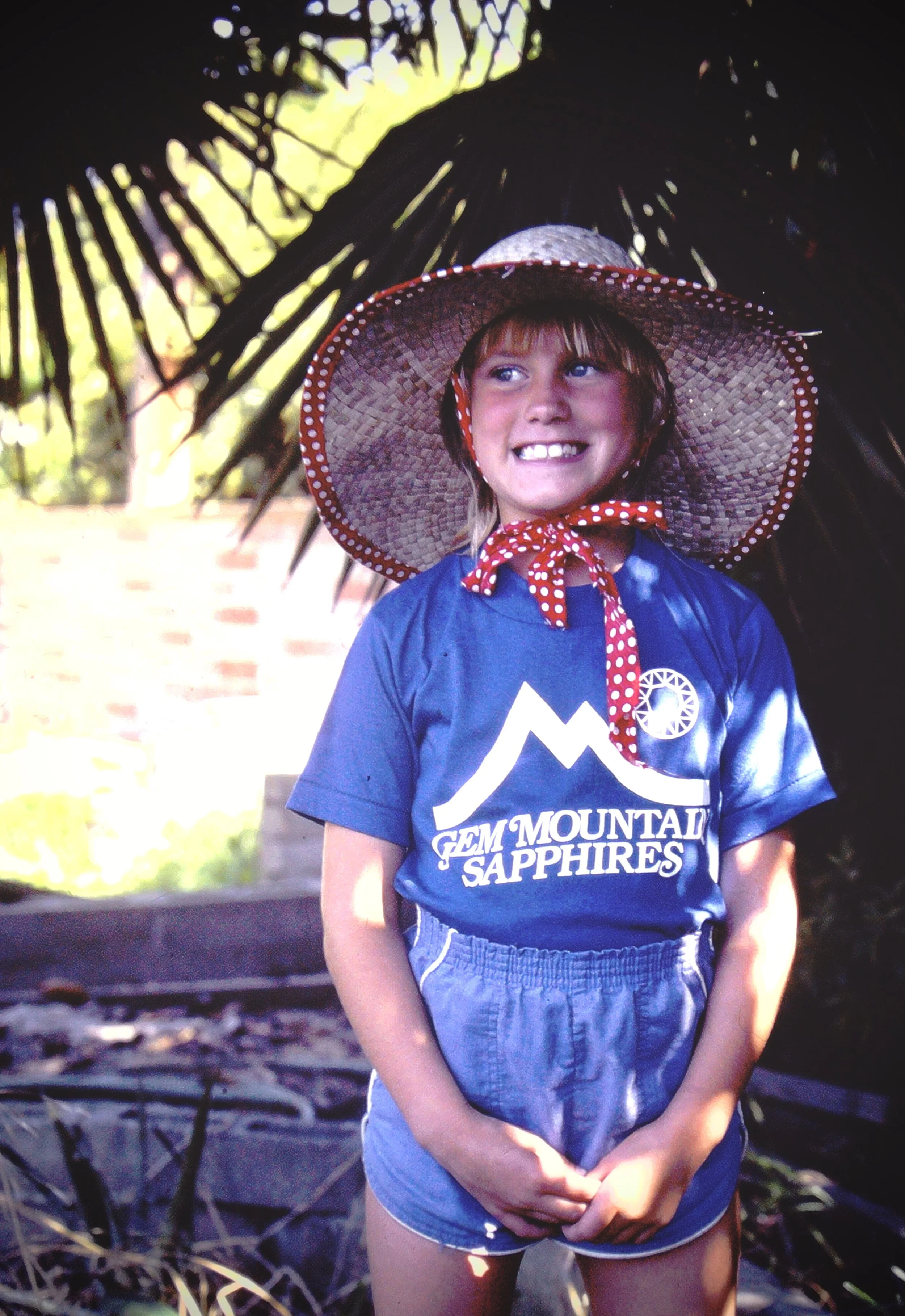 young me with a great big hat, confident grin, and palm trees behind me