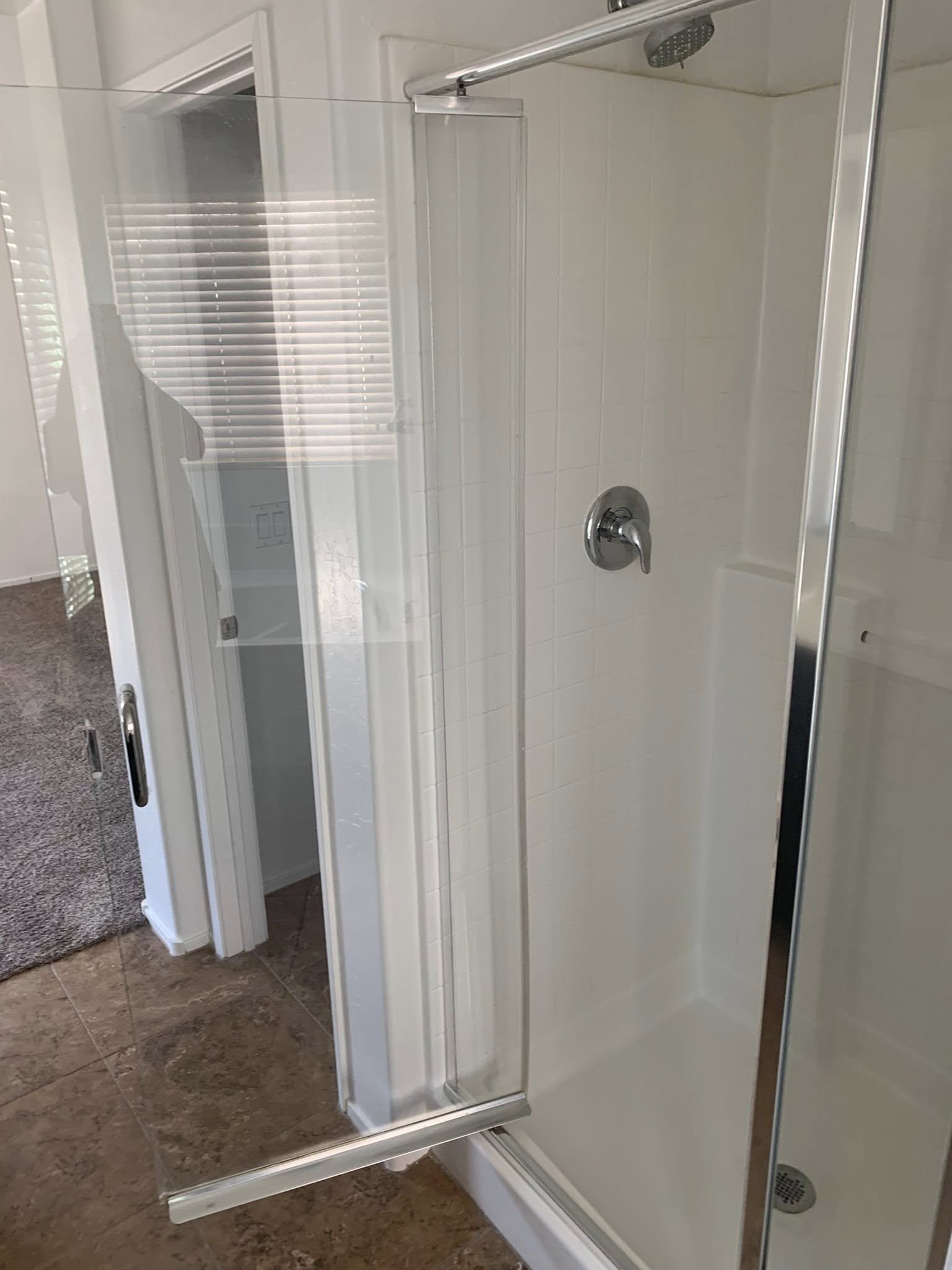 Shower stall with glass door, metal handle, white tiled walls, and a ceiling-mounted shower head.
