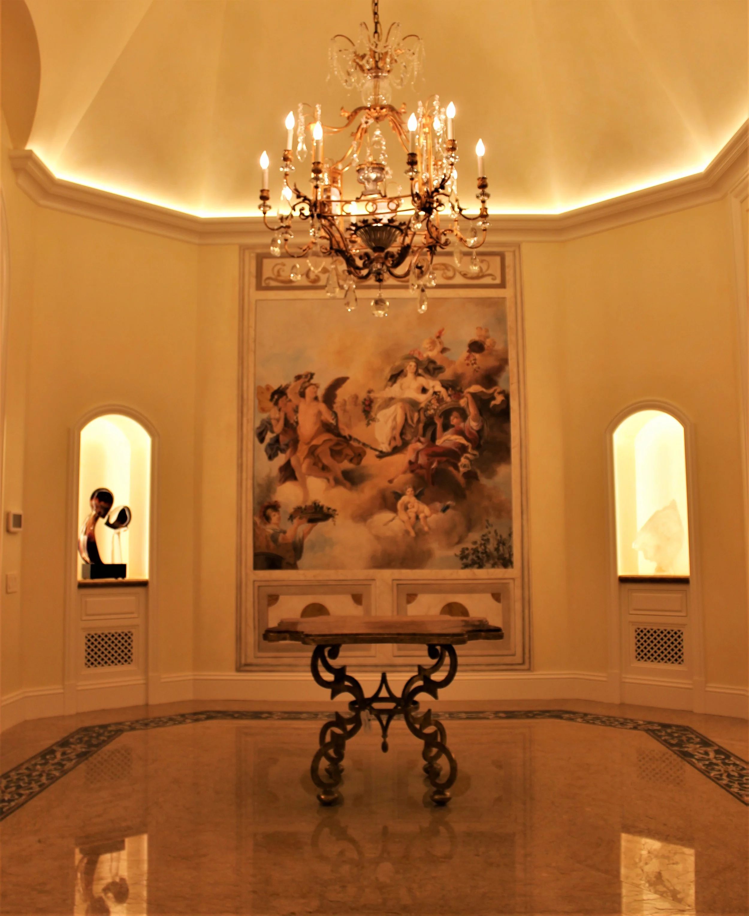 Elegant room with chandelier, ornate table, and classical painting on the wall.