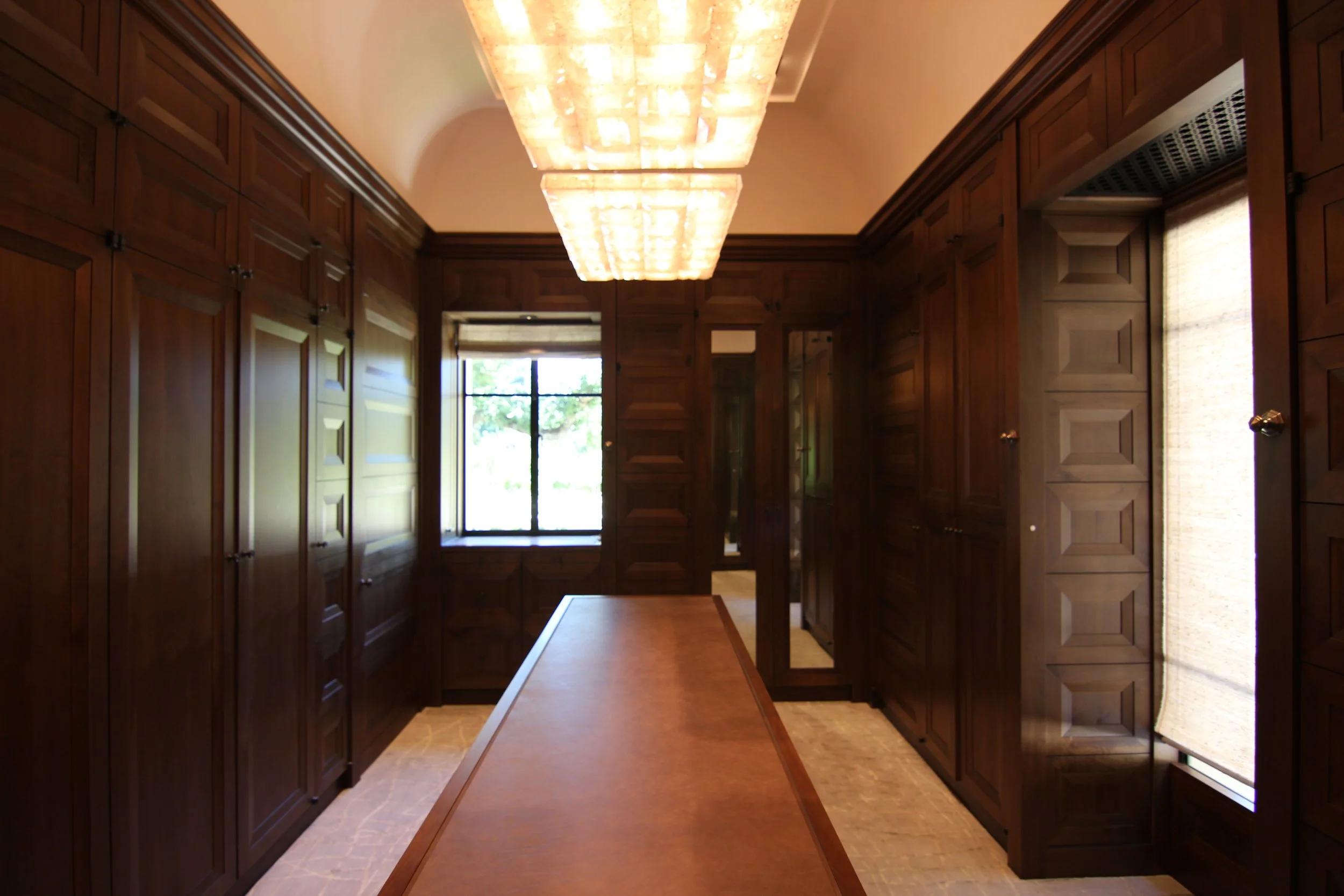 A room with dark wooden paneled walls and a wooden table in the center. There are large windows at the back letting in natural light, and a modern rectangular ceiling light fixture.