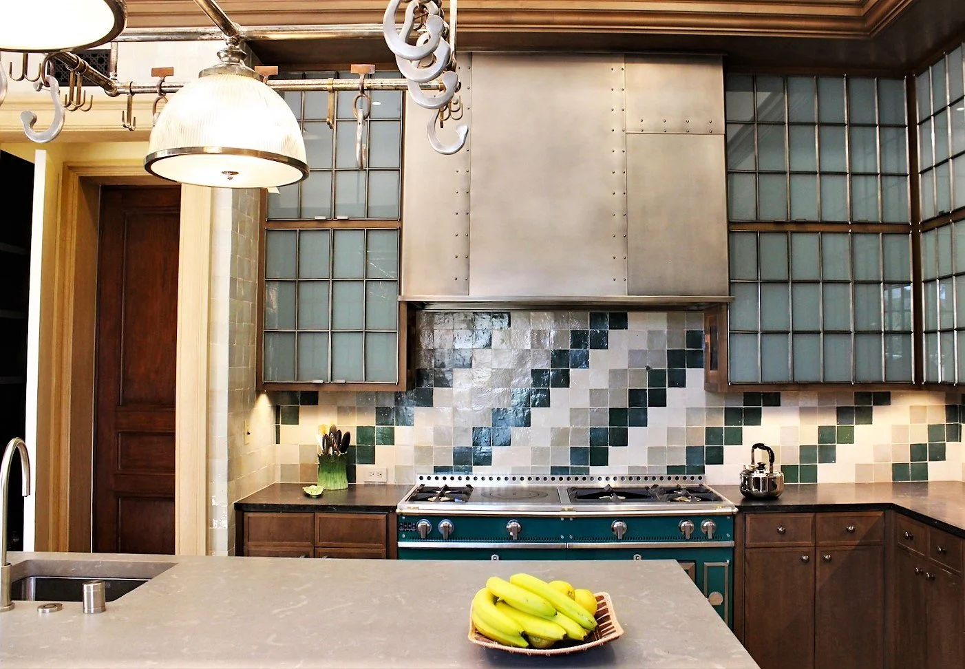 Kitchen with a beige countertop, a bunch of bananas in a basket, a green utensil holder, a gas stove, and glass block windows with wooden framing.