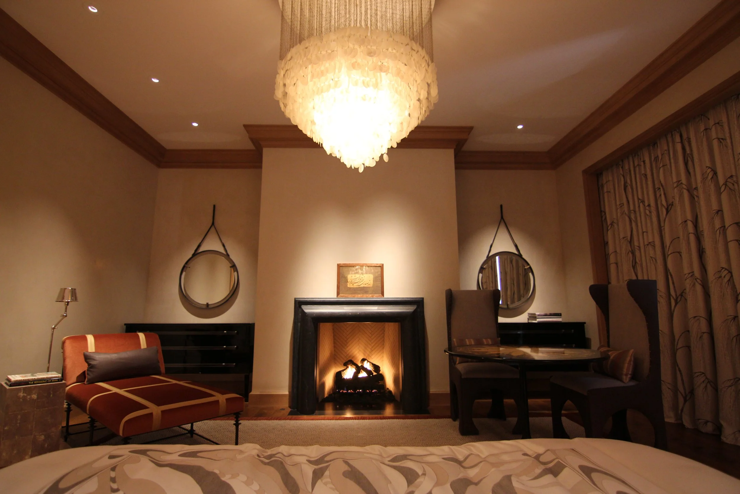 Luxury hotel room with a fireplace, chandelier, mirrors, and elegant furniture.