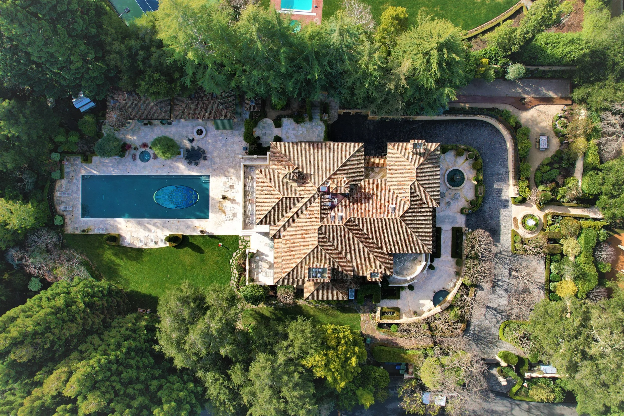 An aerial view of a large house with a swimming pool, surrounding patio, and landscaped yard with trees and greenery.