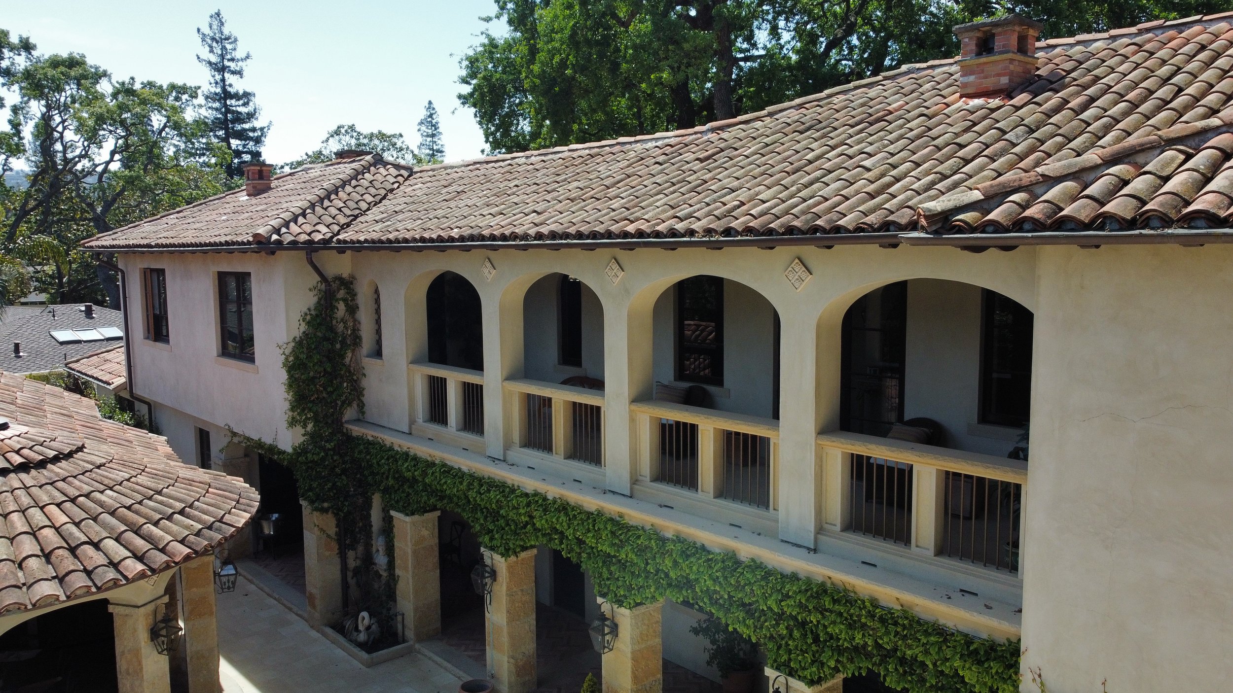 A Mediterranean-style building with a tiled roof, arched balconies, and ivy climbing the walls, surrounded by trees.