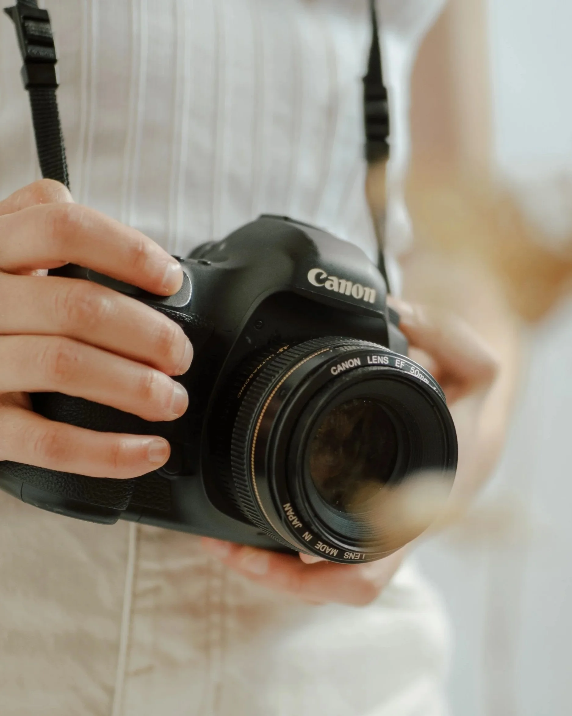 Person holding a black Canon DSLR camera with a 50mm lens.