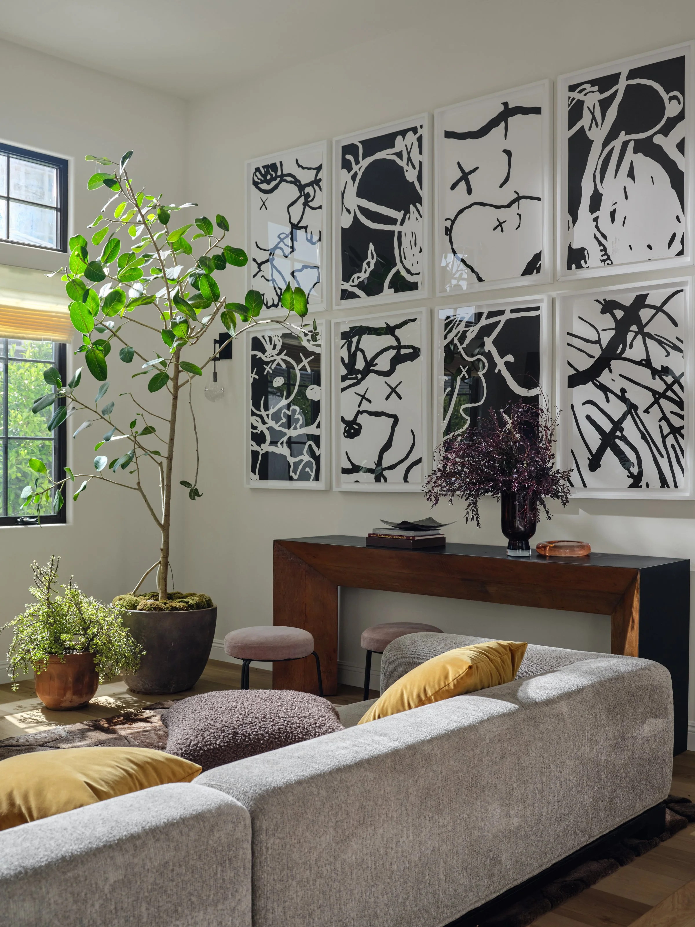 A light-filled living space where bold, graphic artwork becomes the focal point. Layered neutrals, sculptural greenery, rich wood, and unexpected touches of ochre create a collected, artistic feel that is both sophisticated and comfortable.
