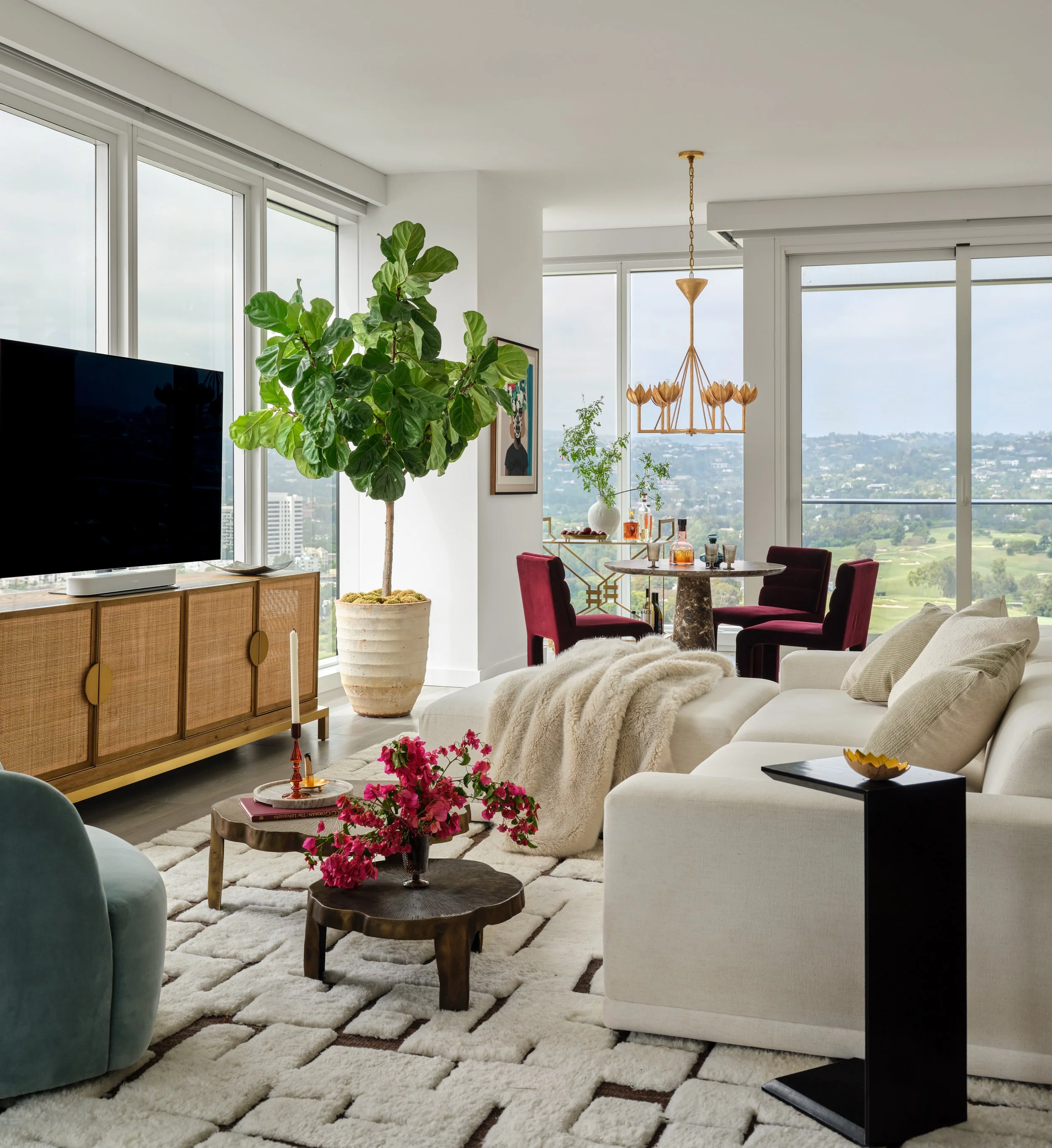 A bright, sophisticated living space designed for both comfort and entertaining. Soft neutral upholstery and a plush textured rug create a relaxed foundation, while sculptural furnishings, rich jewel tones, warm brass accents, and lush greenery bring