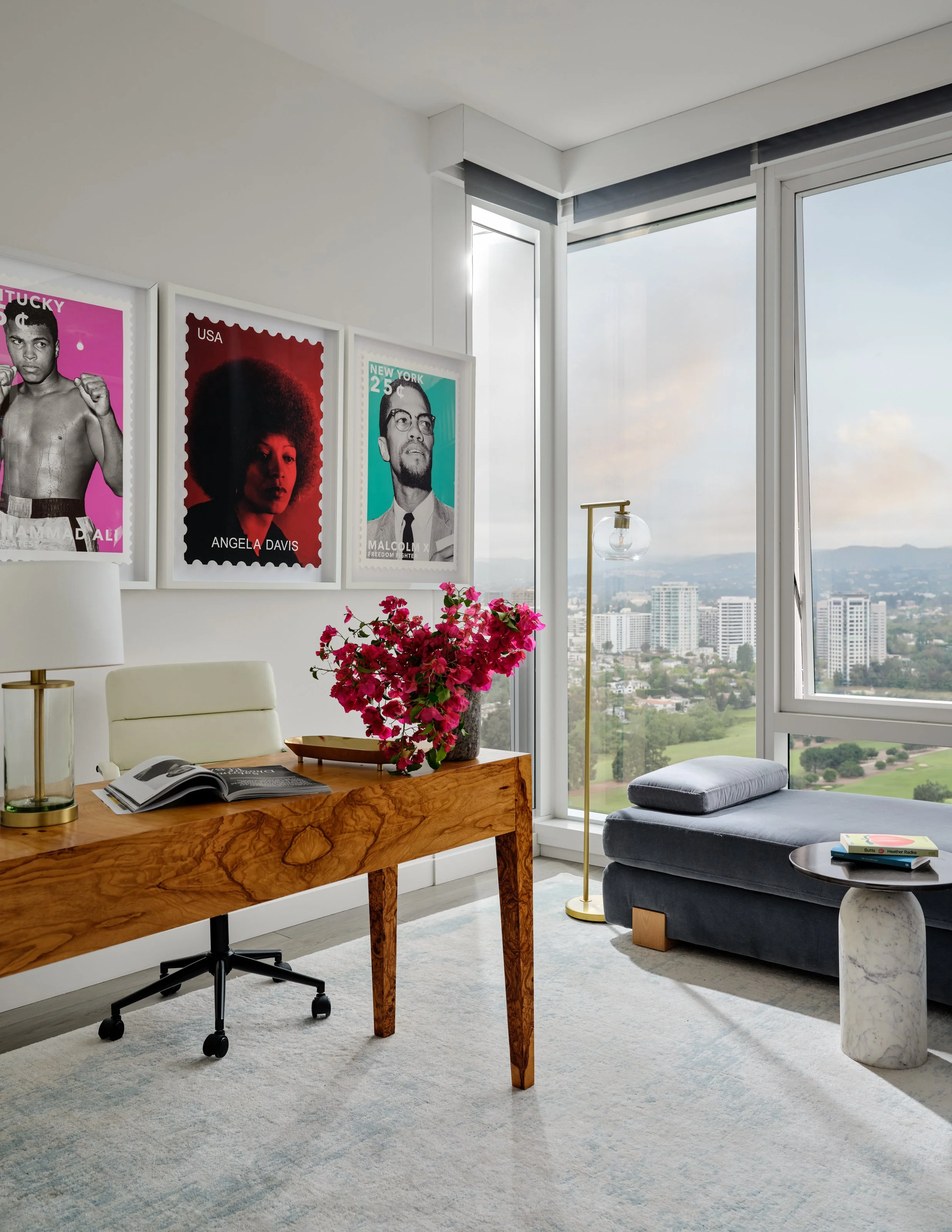 A light-filled home office designed to feel both inspiring and sophisticated. A sculptural wood desk brings warmth and character to the space, while bold artwork, soft textures, and refined brass accents add personality against the expansive city vie