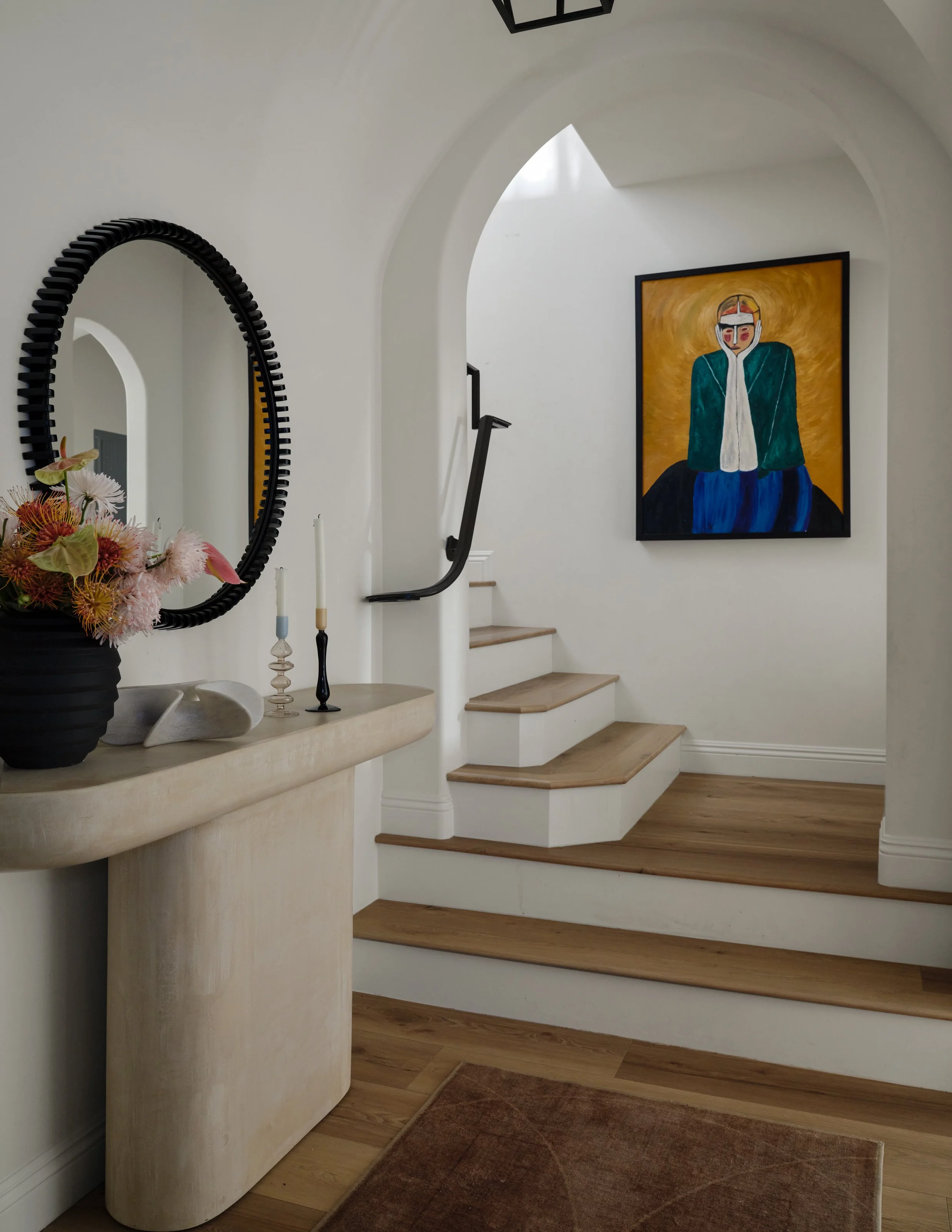 A sculptural entryway where graceful arches and warm natural wood create an inviting sense of arrival. A curved console, statement mirror, and expressive artwork bring personality to the space, balancing architectural softness with bold, collected de