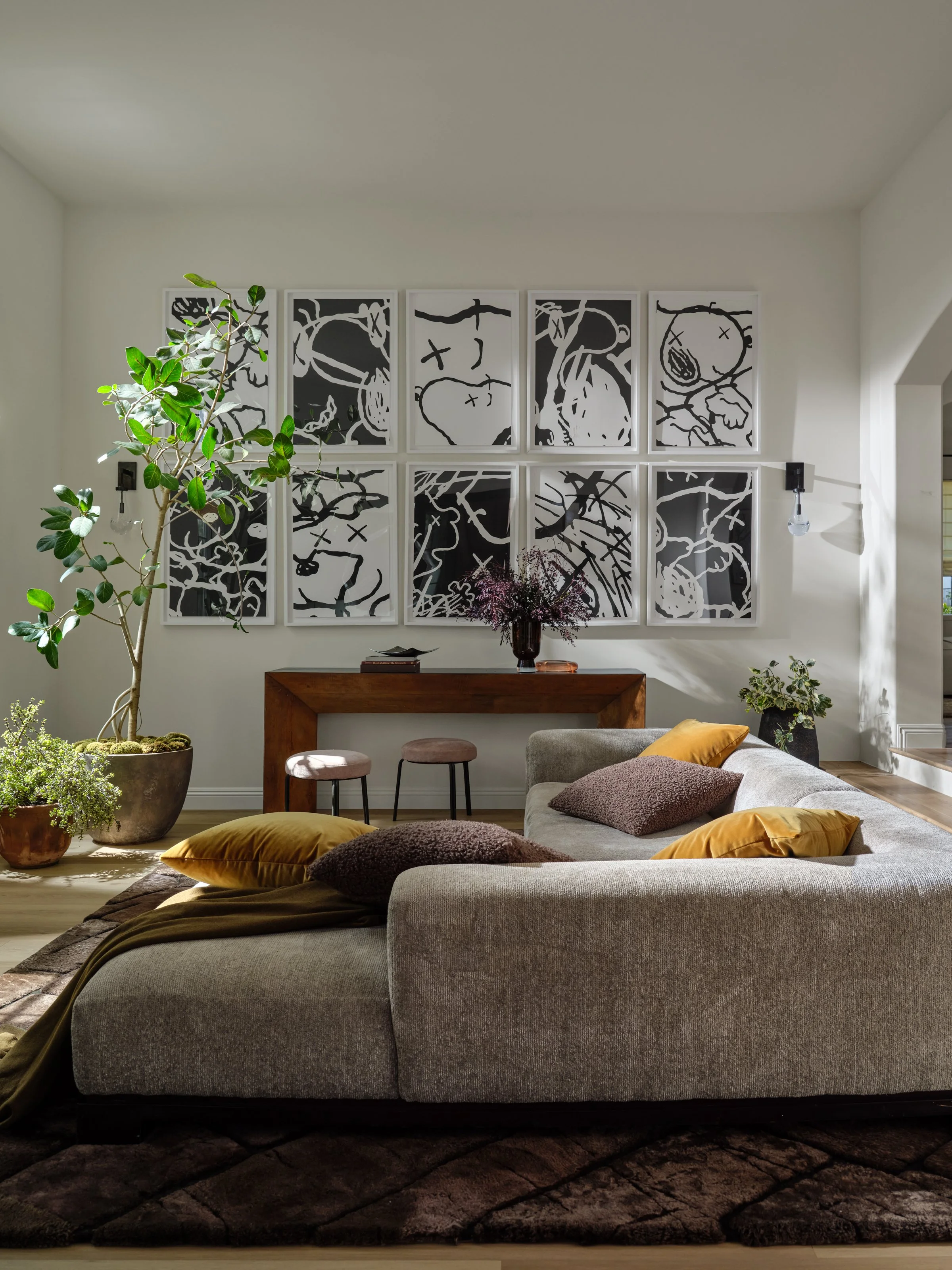 A relaxed living space layered with rich texture, warm earthy tones, and expressive art. The oversized sectional creates an inviting place to gather, while sculptural greenery, natural wood, and touches of ochre bring warmth and personality to the ro