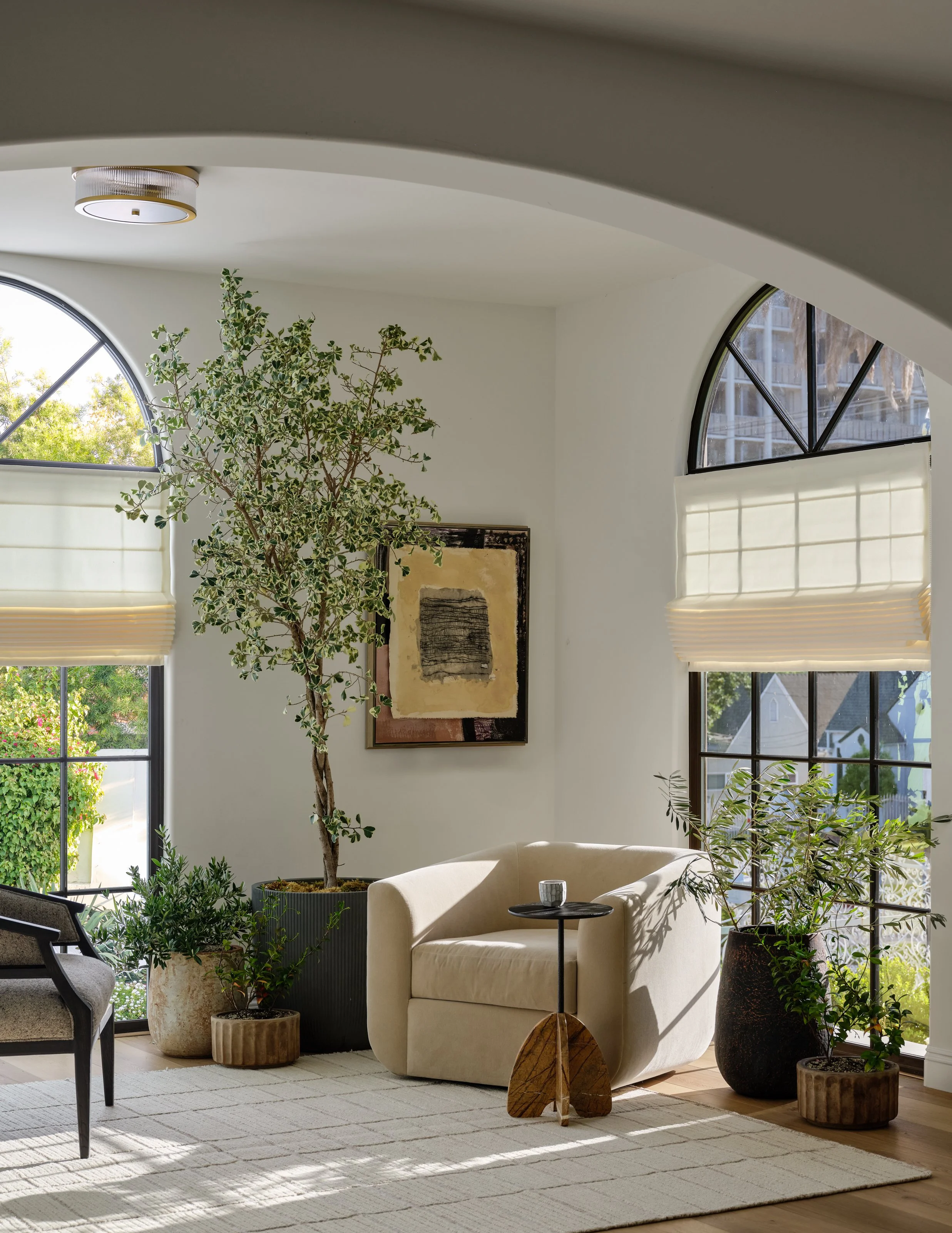 A quiet, sun-filled sitting area that celebrates the home’s architectural curves and connection to nature. Sculptural seating, layered greenery, organic textures, and collected art create an intimate moment that feels serene, refined, and effortlessl