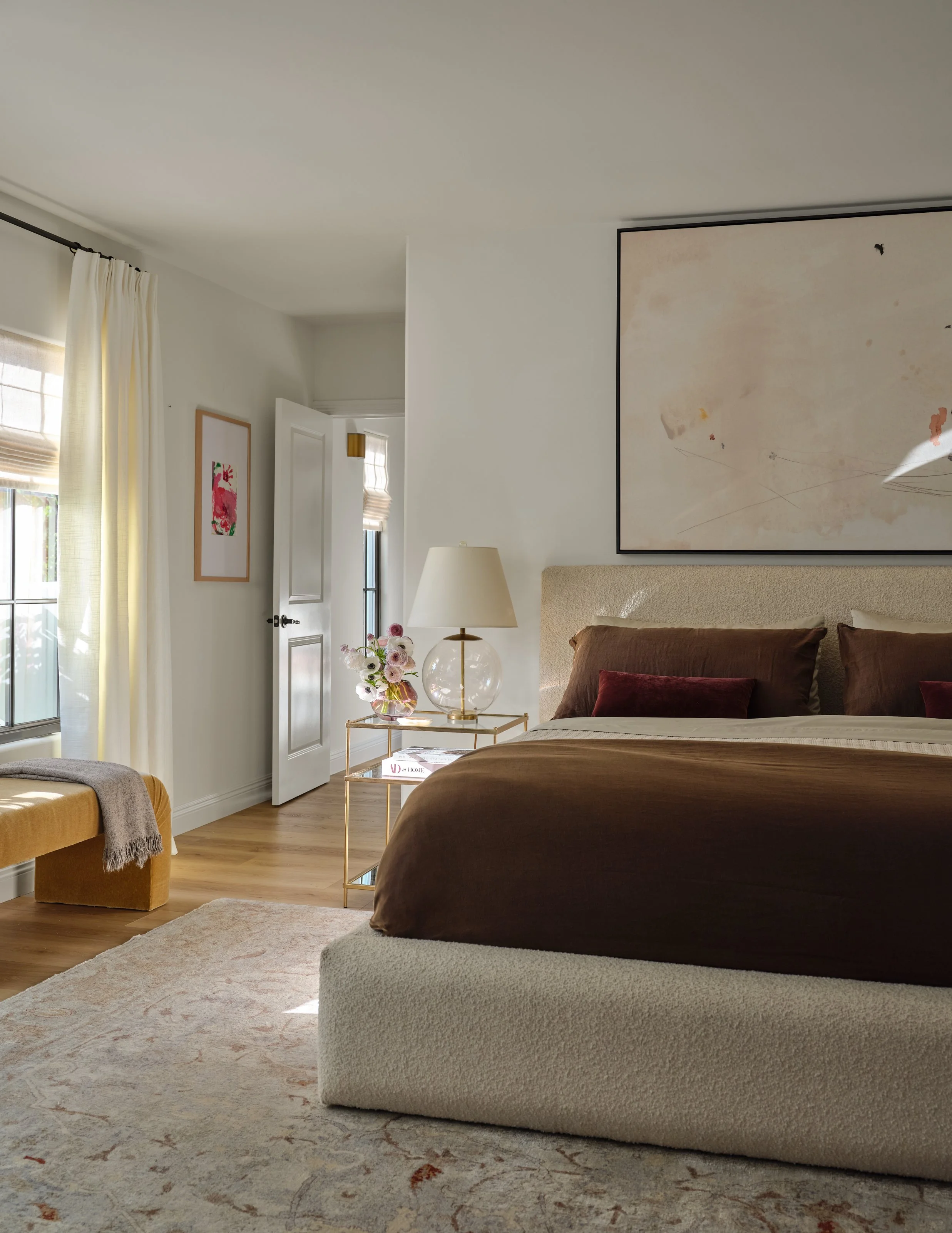 A serene primary bedroom where soft neutrals are layered with rich chocolate and warm ochre tones. Textural fabrics, understated artwork, and natural light create a sophisticated retreat that feels calm, intimate, and effortlessly comfortable.
