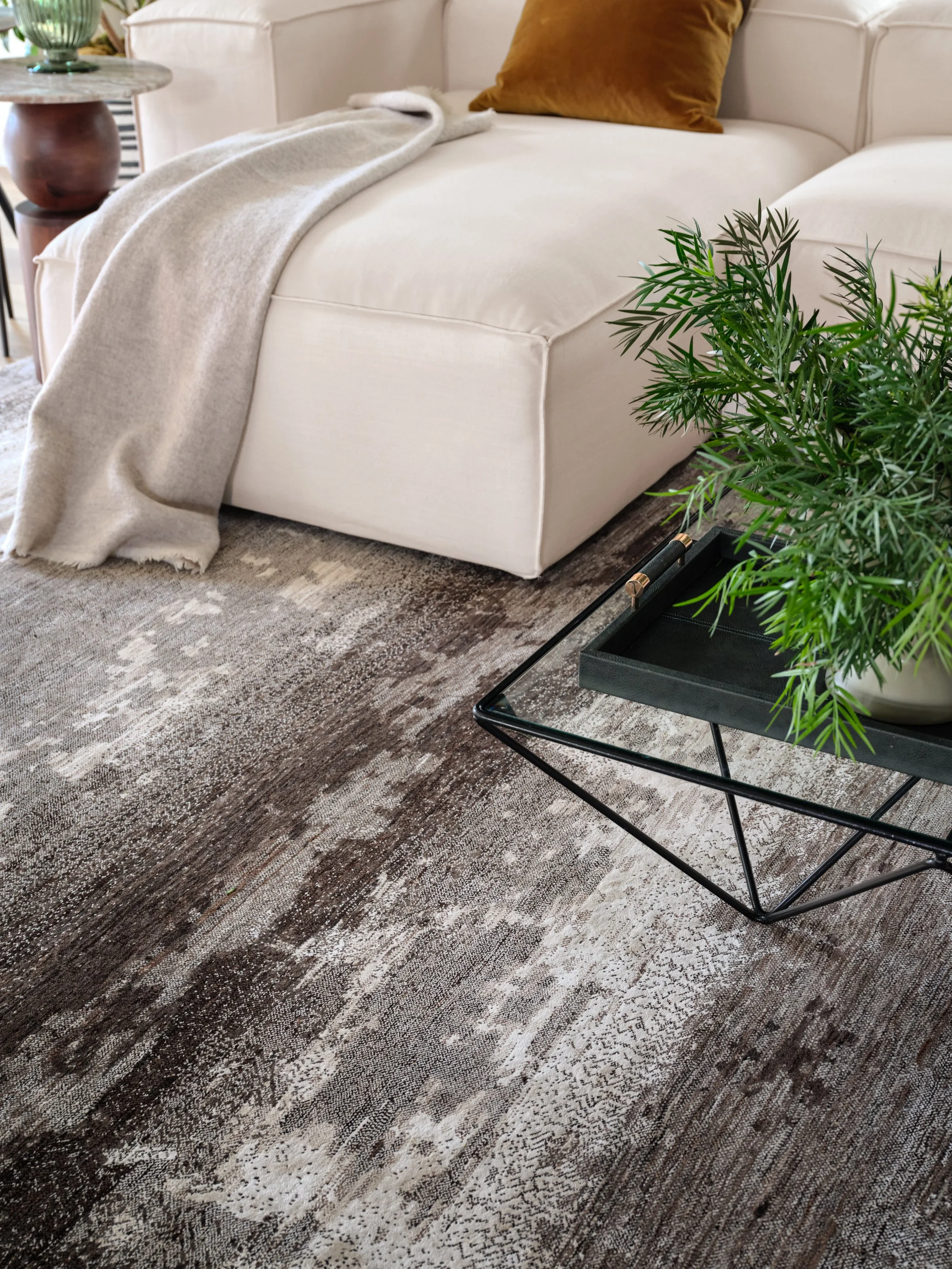 A study in texture and contrast, where soft upholstery, a richly patterned rug, and sculptural accents create depth within a quiet neutral palette. Fresh greenery and a touch of ochre bring warmth and life to this relaxed, thoughtfully layered living