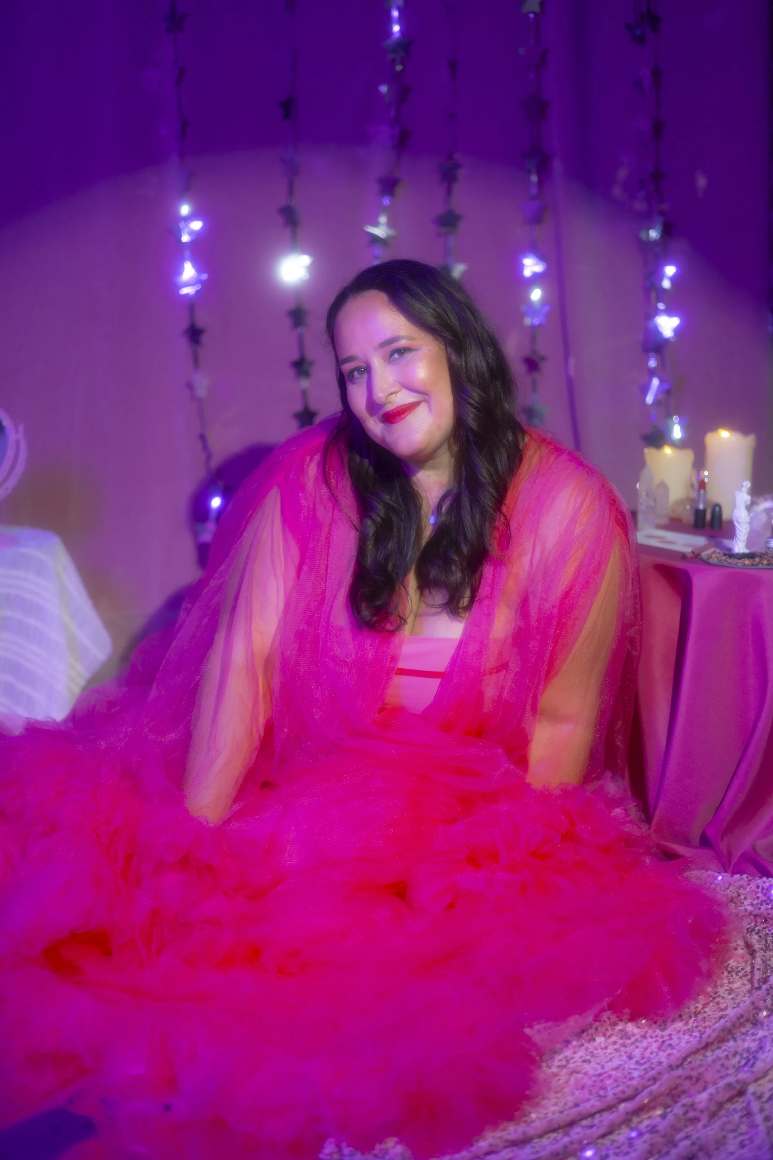 A woman with purple hair, red lipstick, and a black graphic T-shirt smiling at the camera.