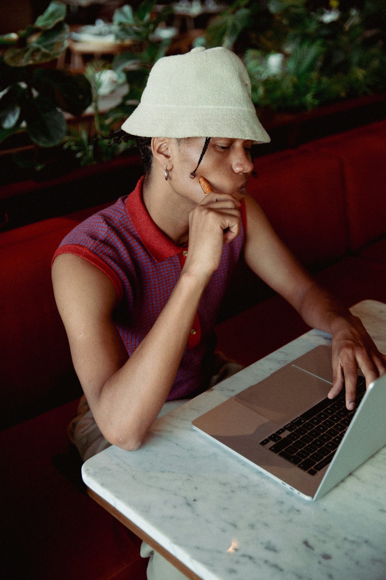A woman relaxing on an orange poolside lounge chair, using her phone with a laptop nearby, beside a swimming pool with orange cushions and trees in the background.