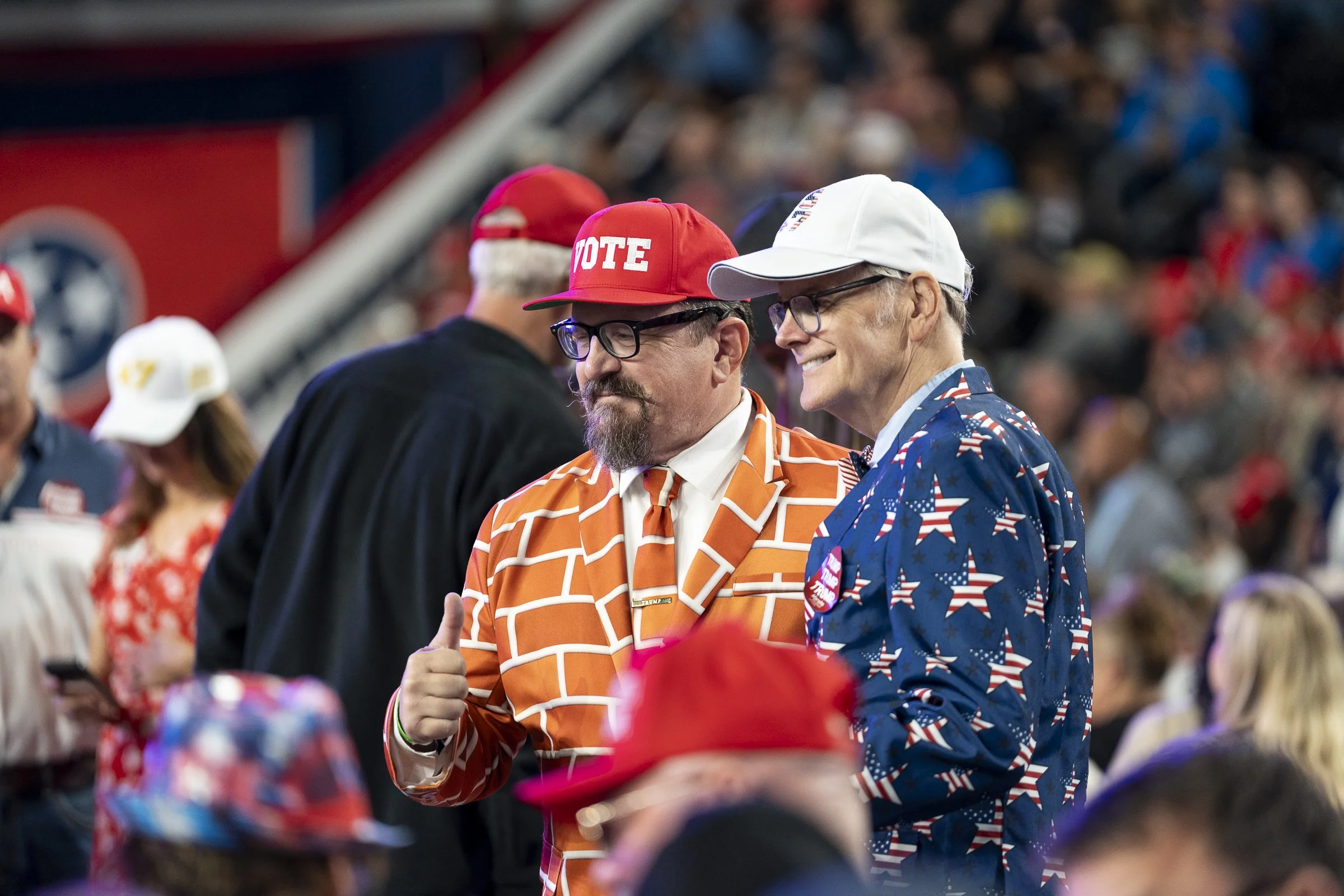  Two attendees pose for a photograph, one wearing an orange-and-white suit in University of Tennessee colors and the other wearing a patriotic stars-and-stripes suit. 