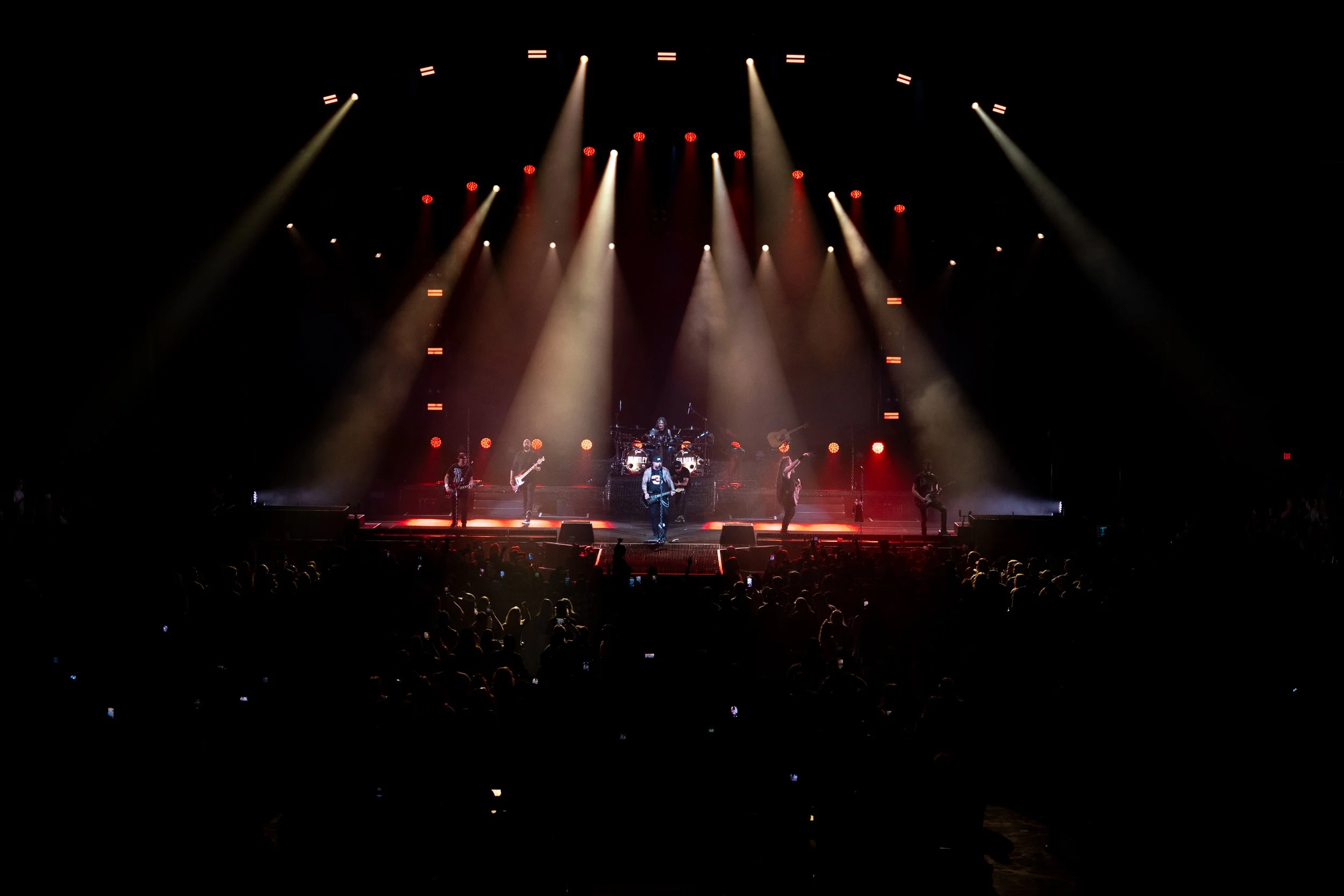 This is an image of a concert stage with musicians performing under bright, colorful stage lights, and an audience watching in the dark.