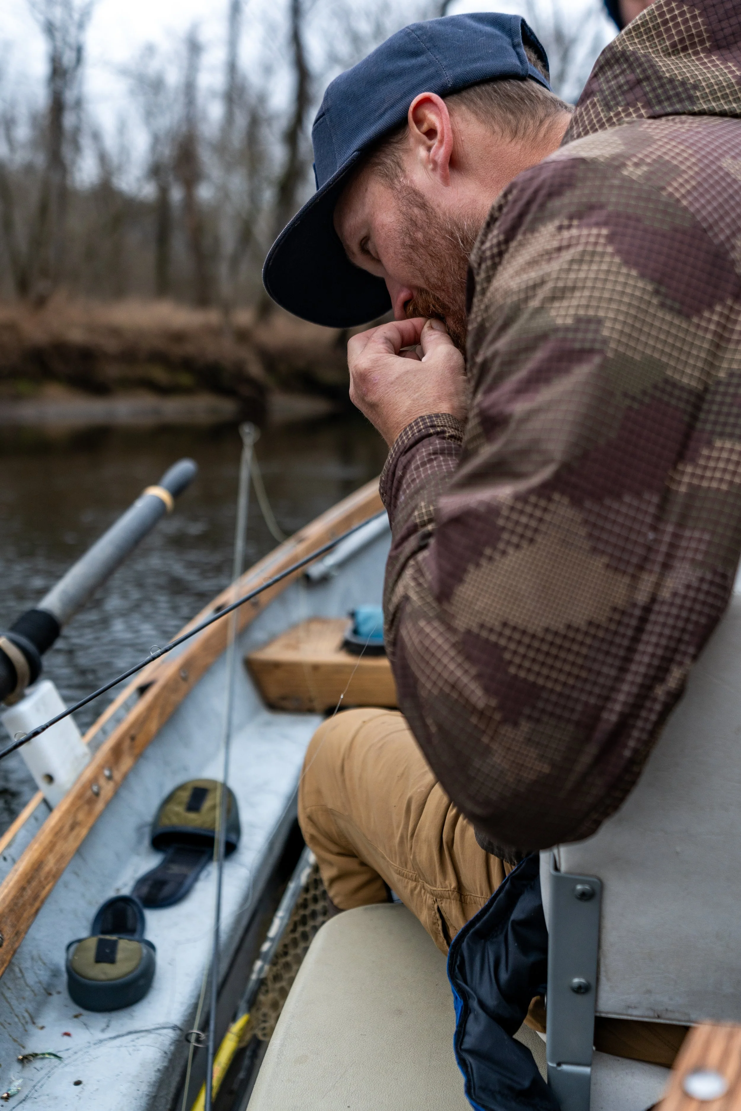 Man in a baseball cap and plaid shirt fishing on a boat in a river or lake.