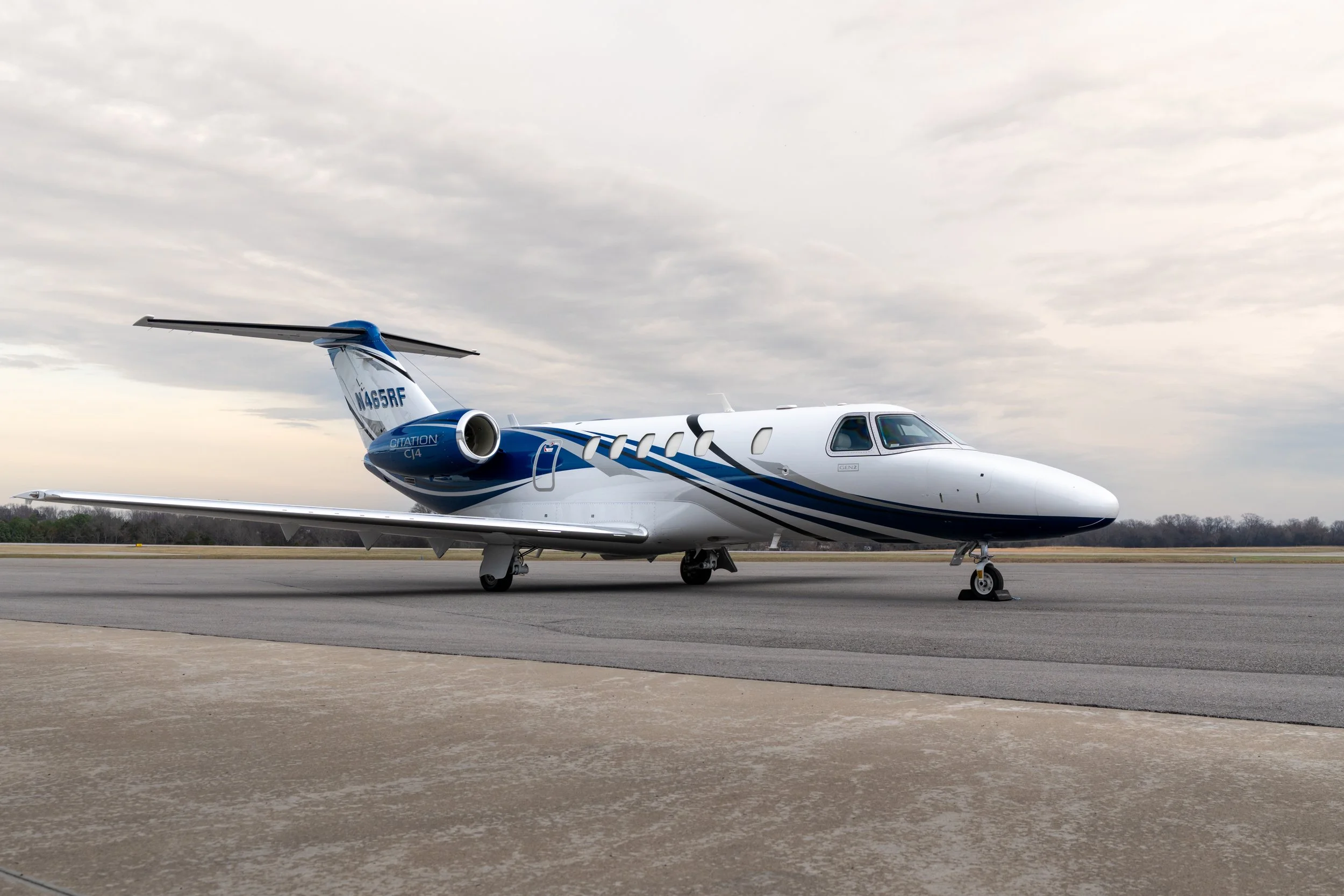 A sleek white private jet with blue accents parked on a tarmac under a cloudy sky.