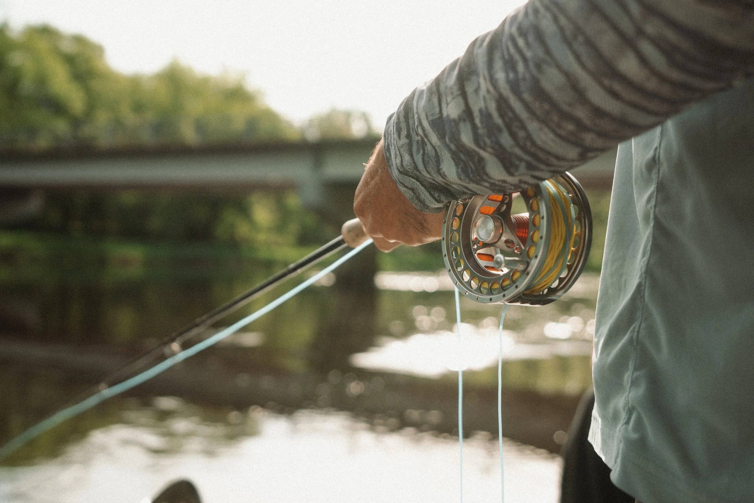 Close-up of a person holding a fishing reel on a boat with water and trees in the background.