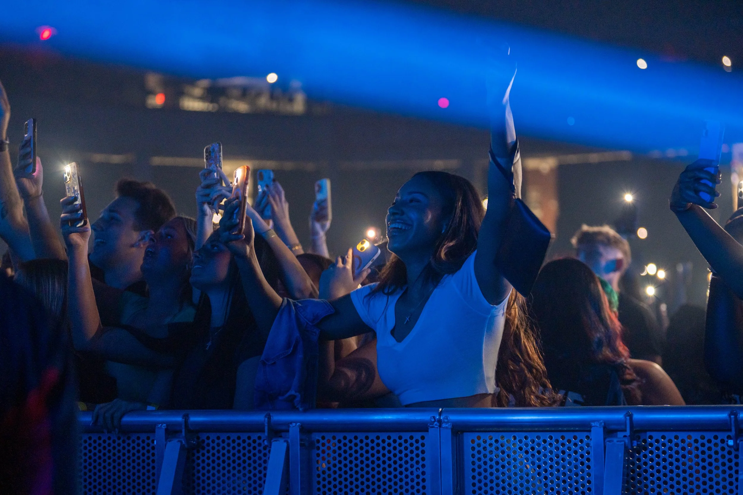 Crowd of people at a concert, taking photos and videos with their smartphones, illuminated by blue stage lighting.