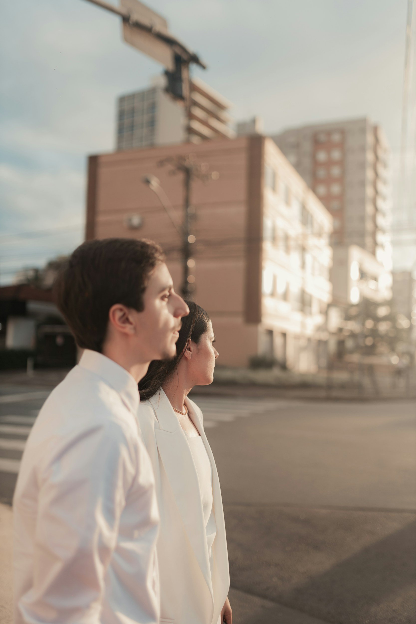 Three individuals standing in profile outdoors in business attire with city buildings and a clear sky in the background during late afternoon or early evening.