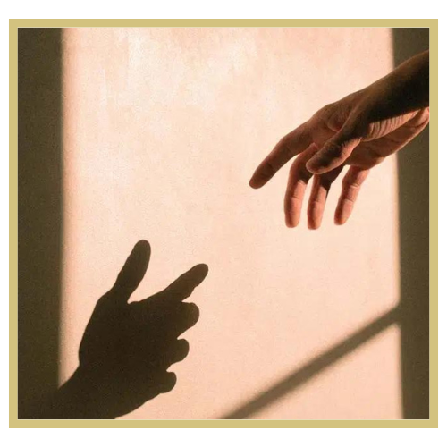 Shadow of a hand making a peace sign and a person's hand reaching out, with a soft pink background and natural lighting.
