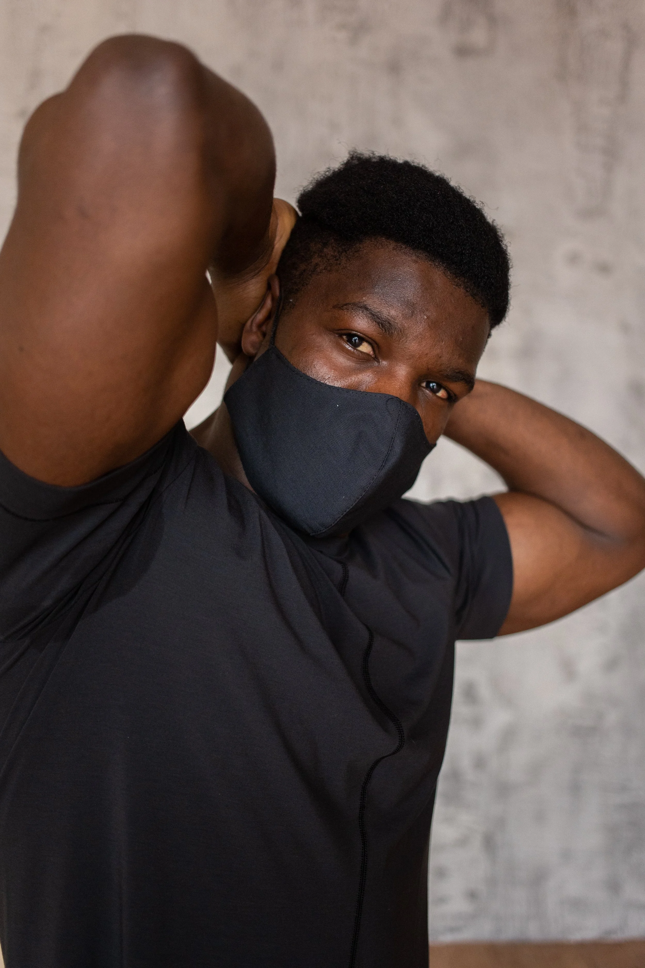 African American man wearing a black t-shirt adjusting his mask.