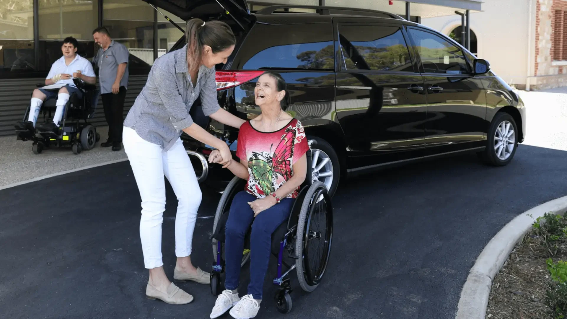 Support worker assisting woman in a wheelchair beside an accessible vehicle.