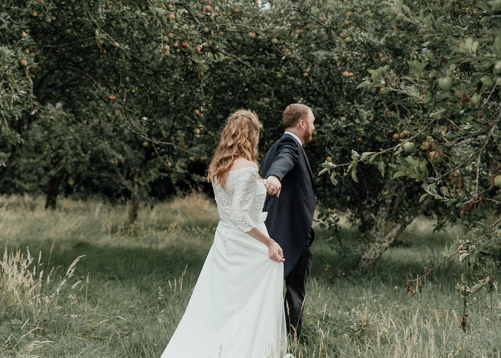 orchard outdoor wedding groom leads bride off hand in hand