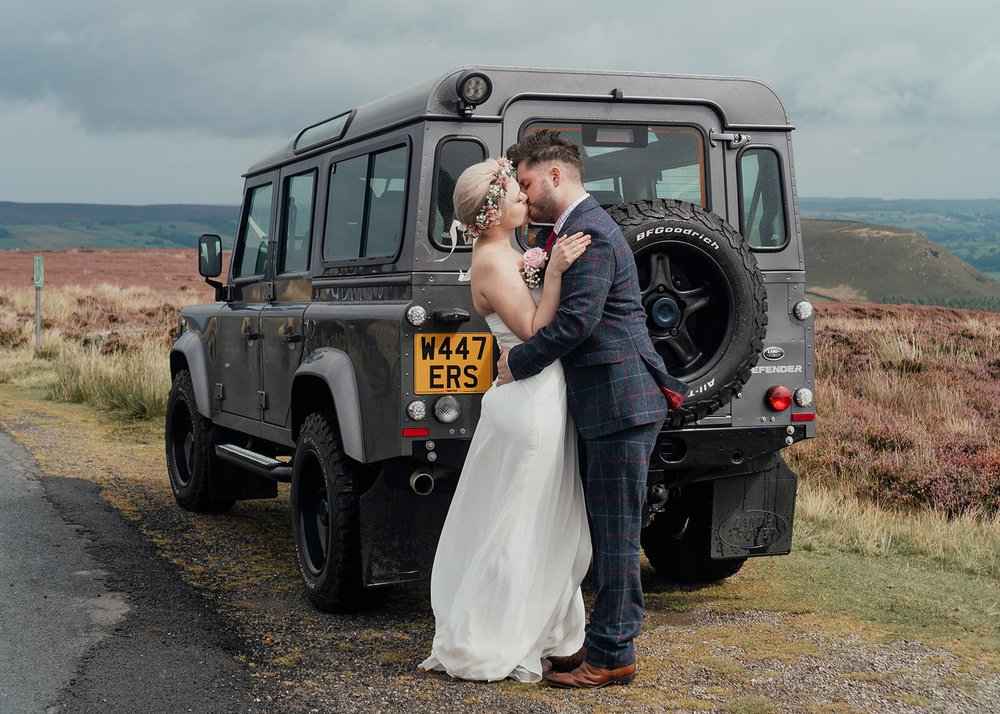 couple kiss on north york moors in front of landrover defender wedding car