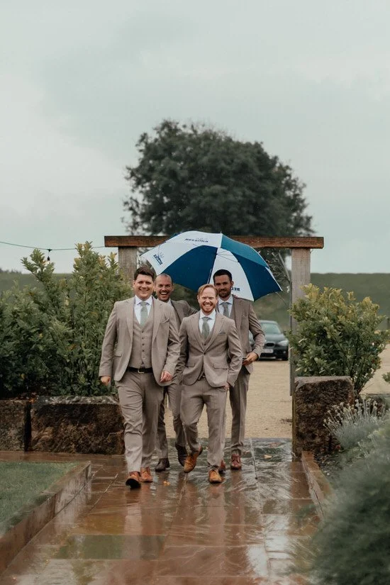 groomsmen walking into Eden Barn wedding venue in the rain with umbrellas
