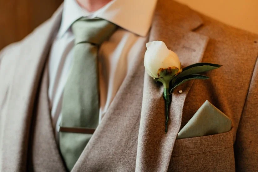 close up of a grooms sage green tie and white peony buttonhole