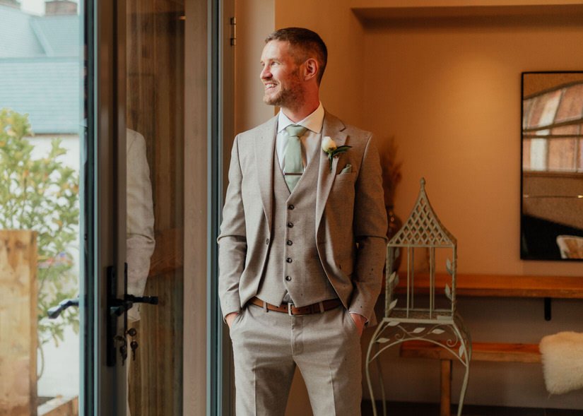 groom ready for his wedding ceremony, looking out a window, with hands in his pockets
