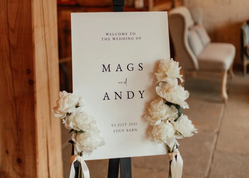 white wedding welcome sign with black writing and white peonies decorating each side