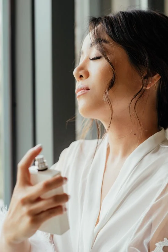 bride spraying perfume on her neck with her eyes closed