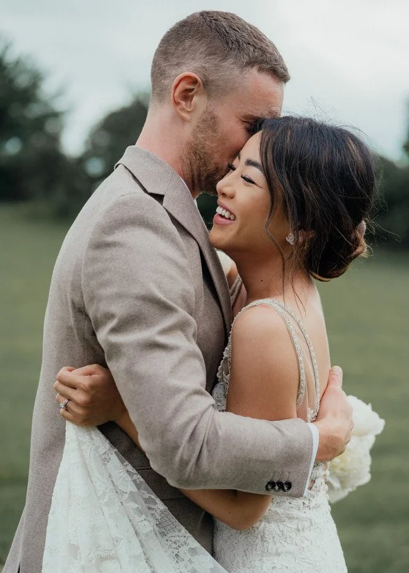 bride and groom hugging and smiling, with the bride's lace dress wrapped around them