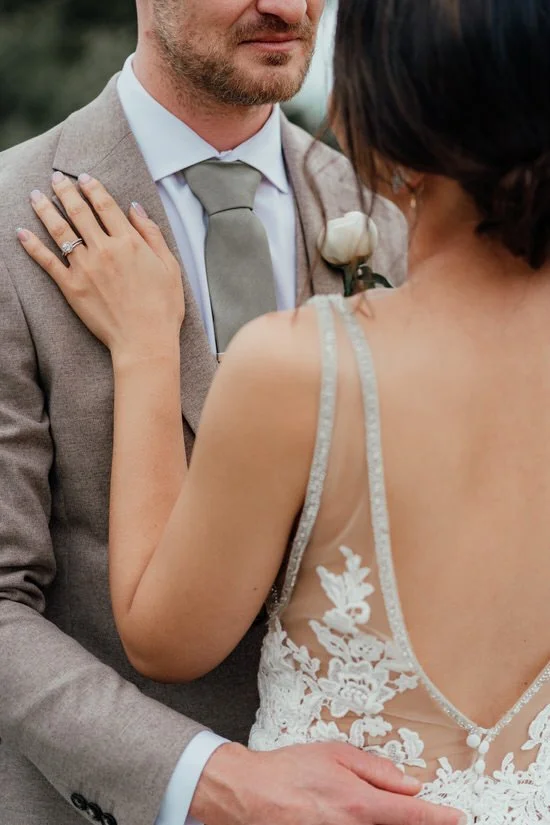 back of a bride's dress with her hand and wedding ring on the groom's chest