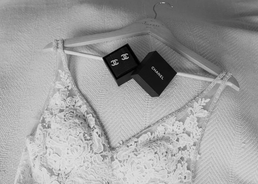 Chanel earrings in a black box with a wedding dress on a bridal hanger, in black and white